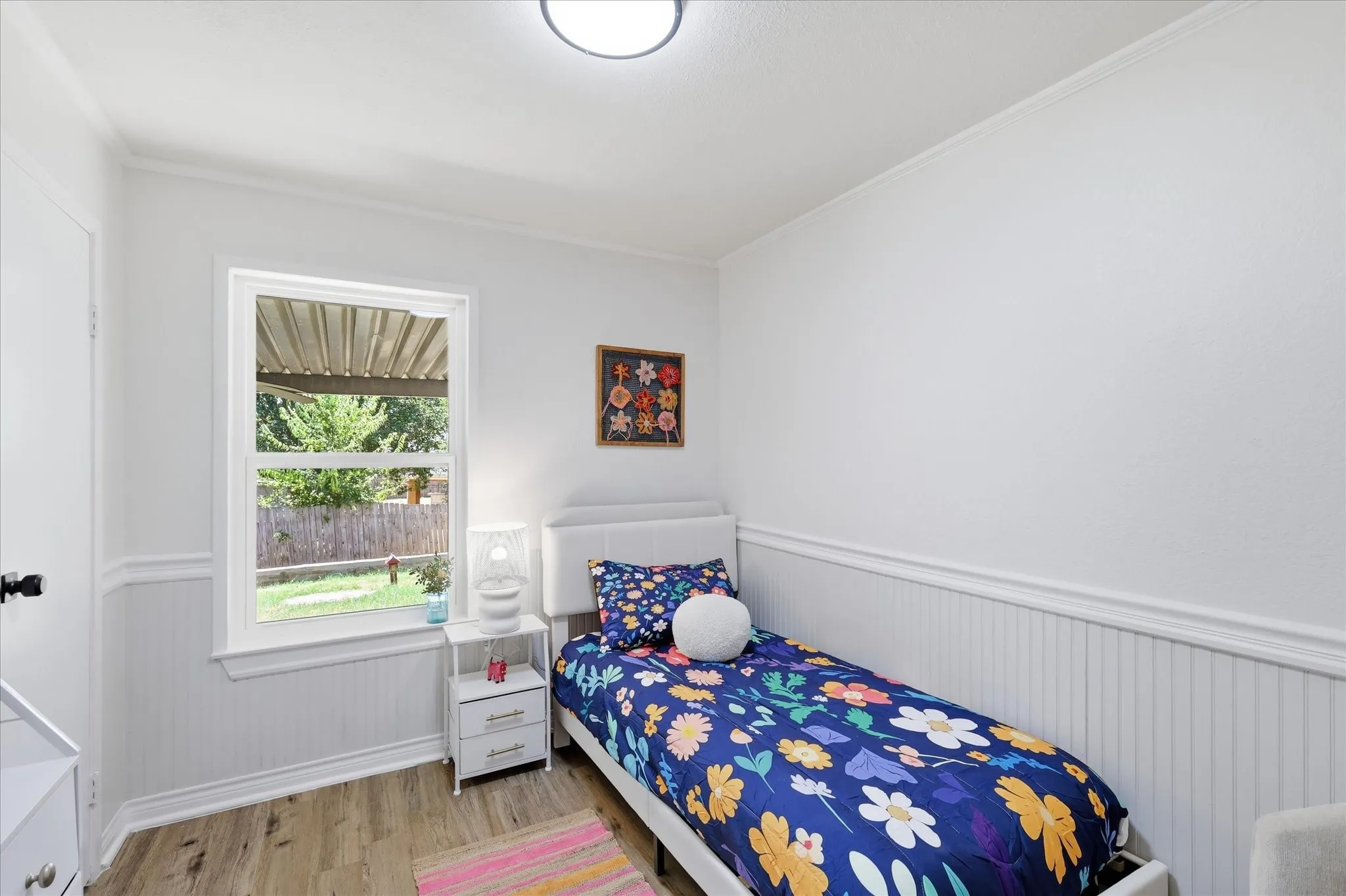 White walls with wainscoting, wood-finish flooring, and a single window