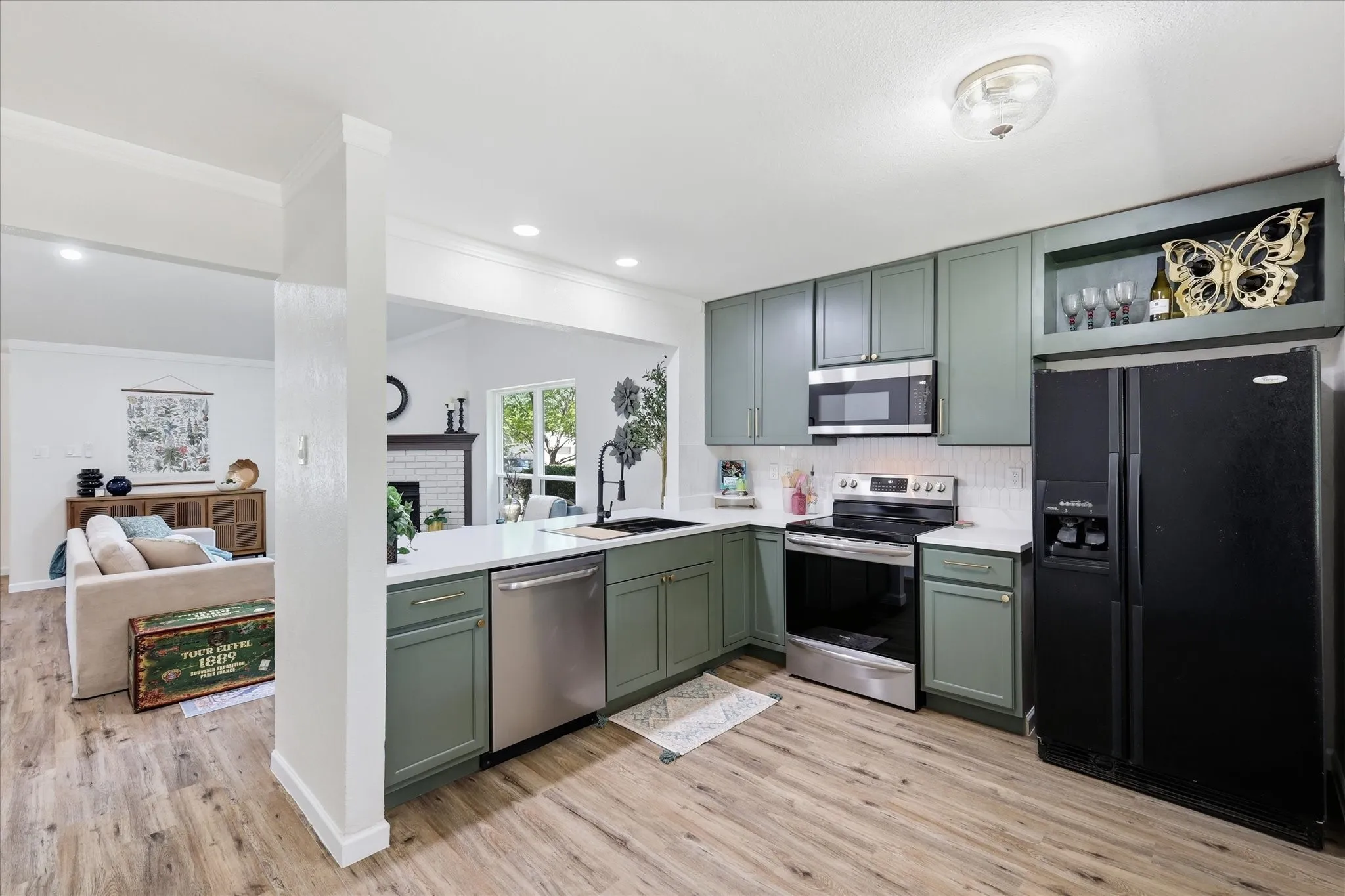 L-shaped kitchen with green cabinetry, stainless steel appliances, white countertops, and wood-finish flooring
