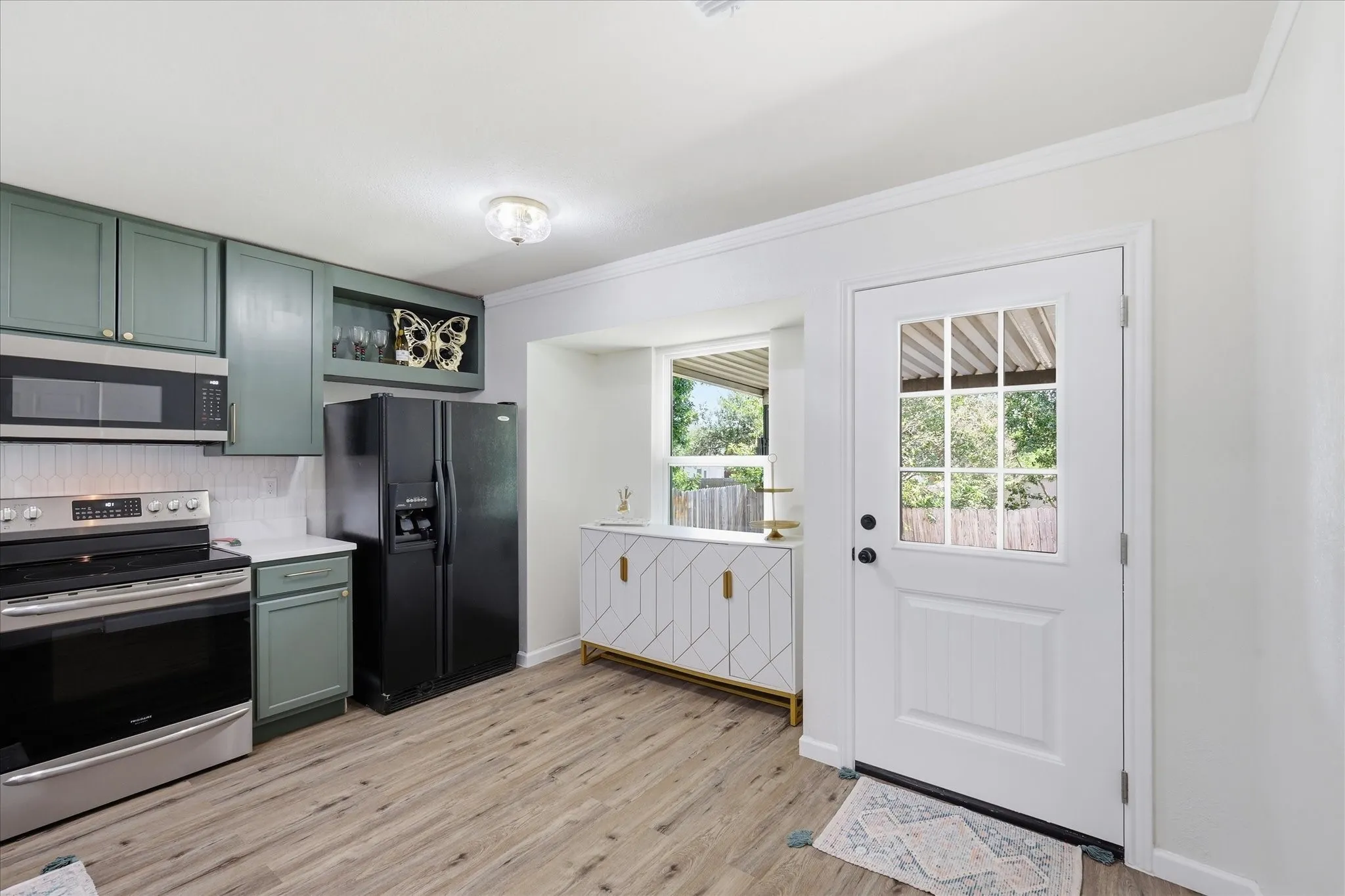 Wood-finish flooring, contemporary kitchen cabinetry, stainless steel range with overhead microwave, black refrigerator, and a white paneled door with glass inserts