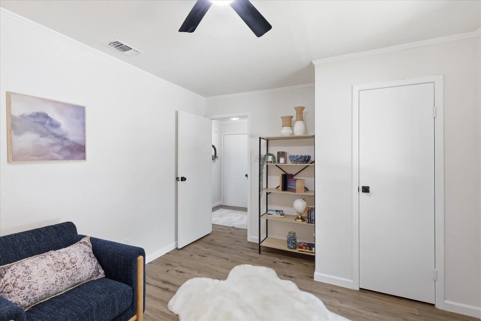 Wood-finish flooring with white baseboards, a white ceiling with crown molding, and a black ceiling fan