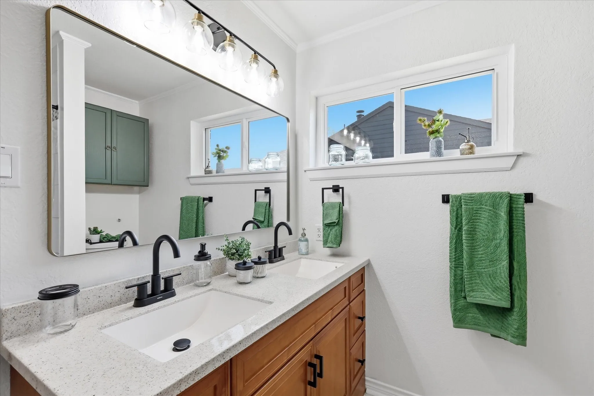 Double vanity with integrated sinks, light-toned countertop, wood-finish cabinetry, and matte black fixtures