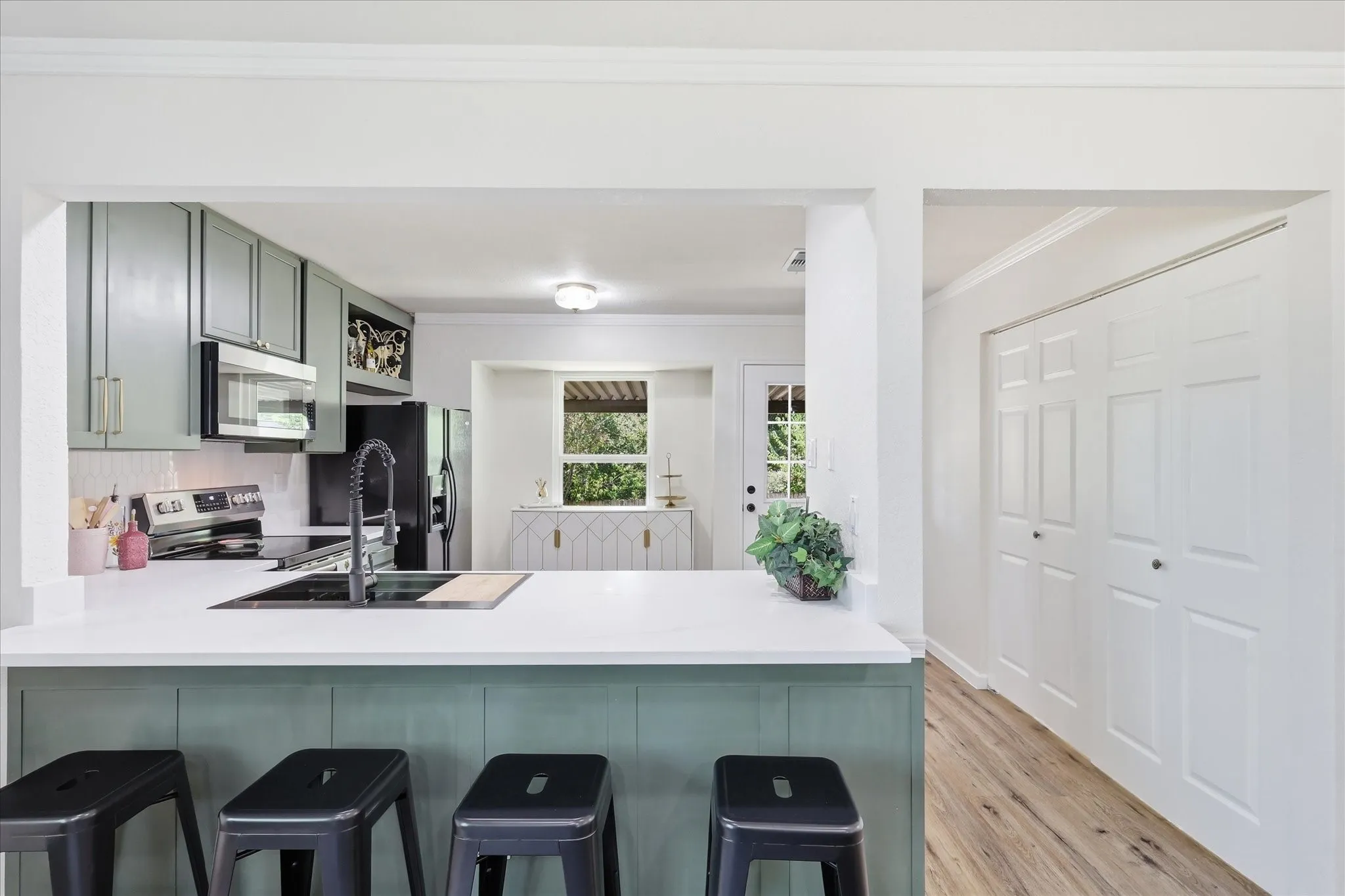 Kitchen featuring an undermount sink with a black gooseneck faucet, light green cabinetry, white countertops, and stainless steel appliances