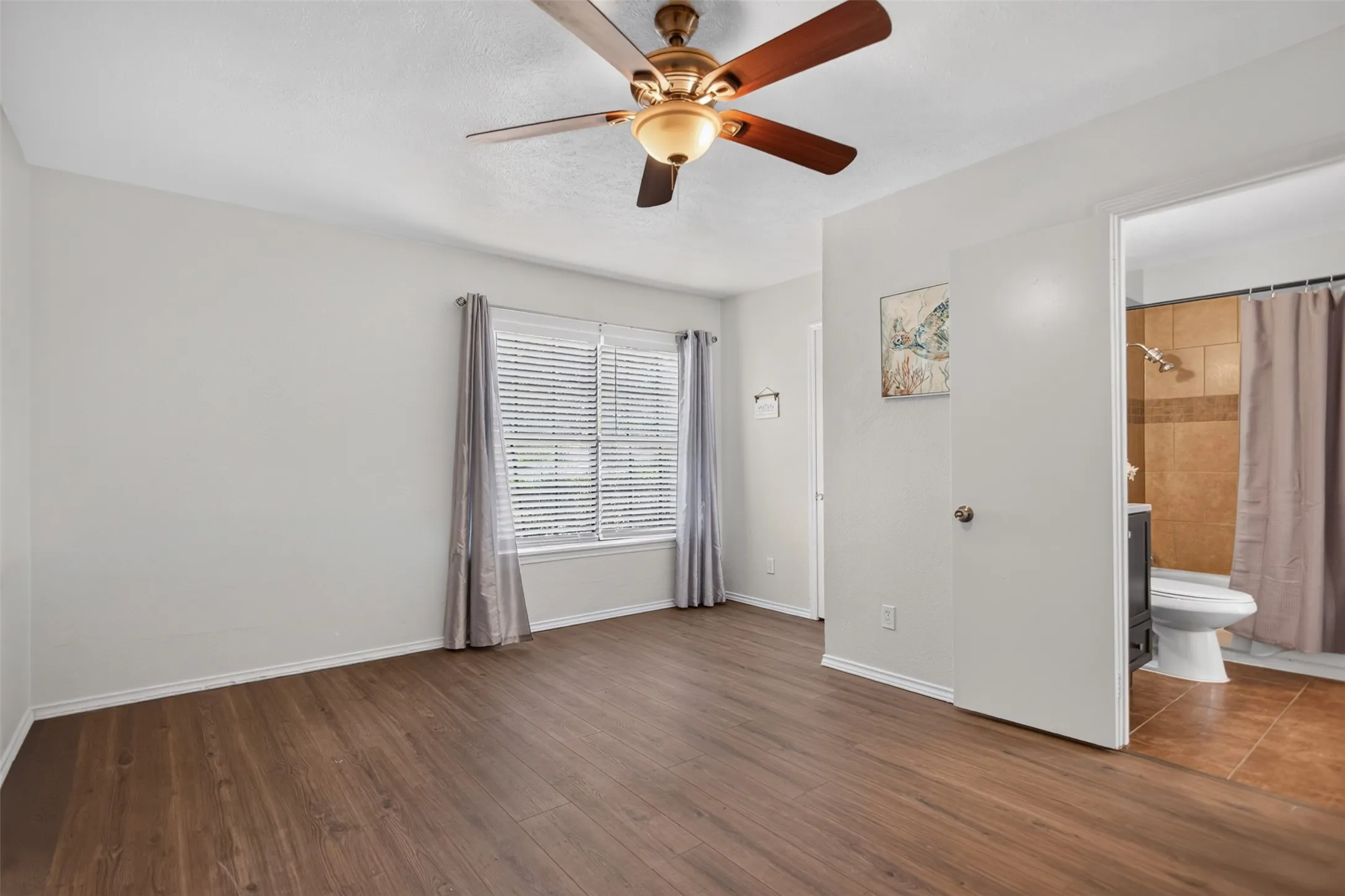 view of bedroom and bathroom, ceiling fan, window treatments, new flooring