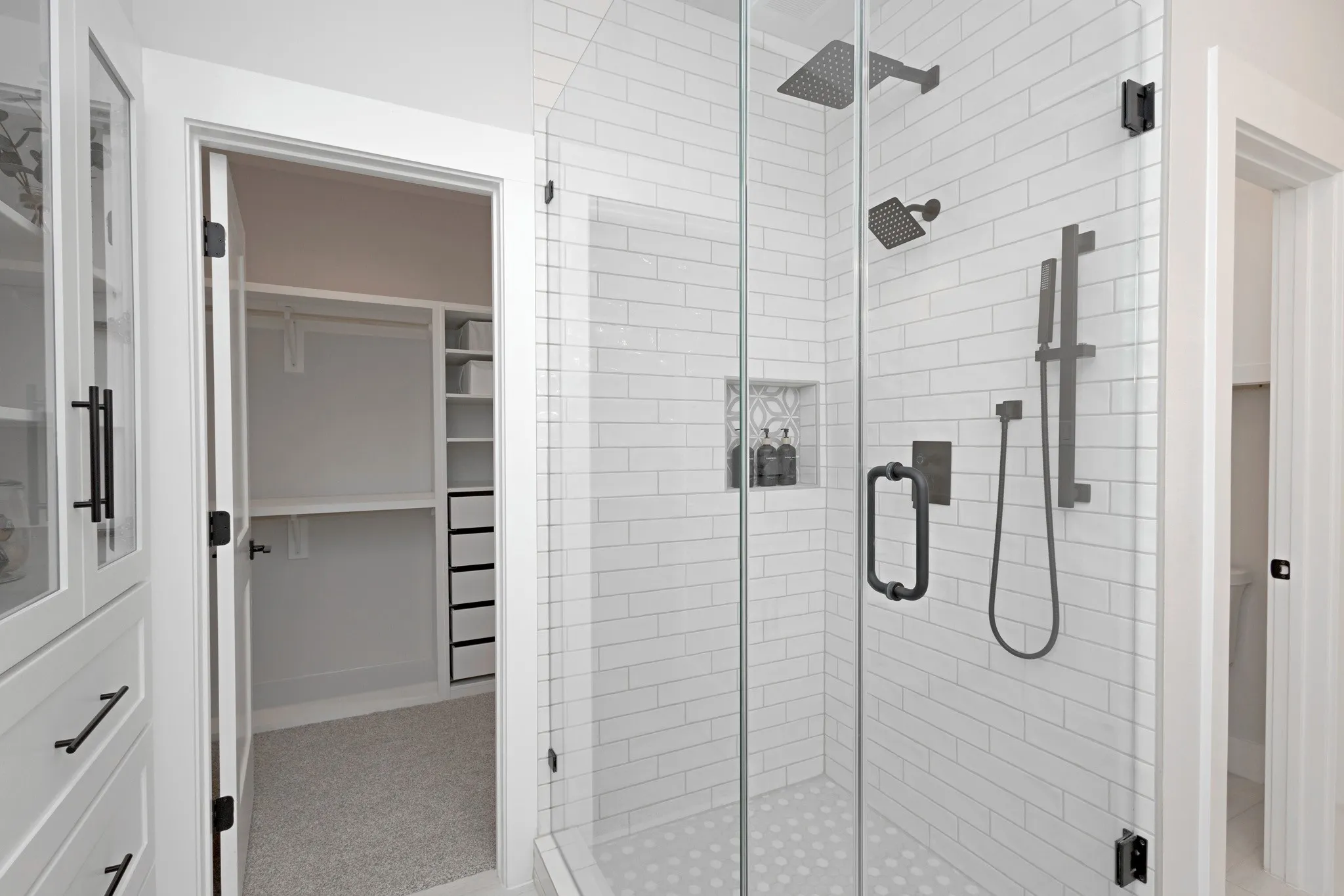 A Frameless Glass Shower with a Luxury Dual Shower Head System and a Built-In Custom Cabinet with Glass Doors and Deep Drawers elevate the spa-like experience.