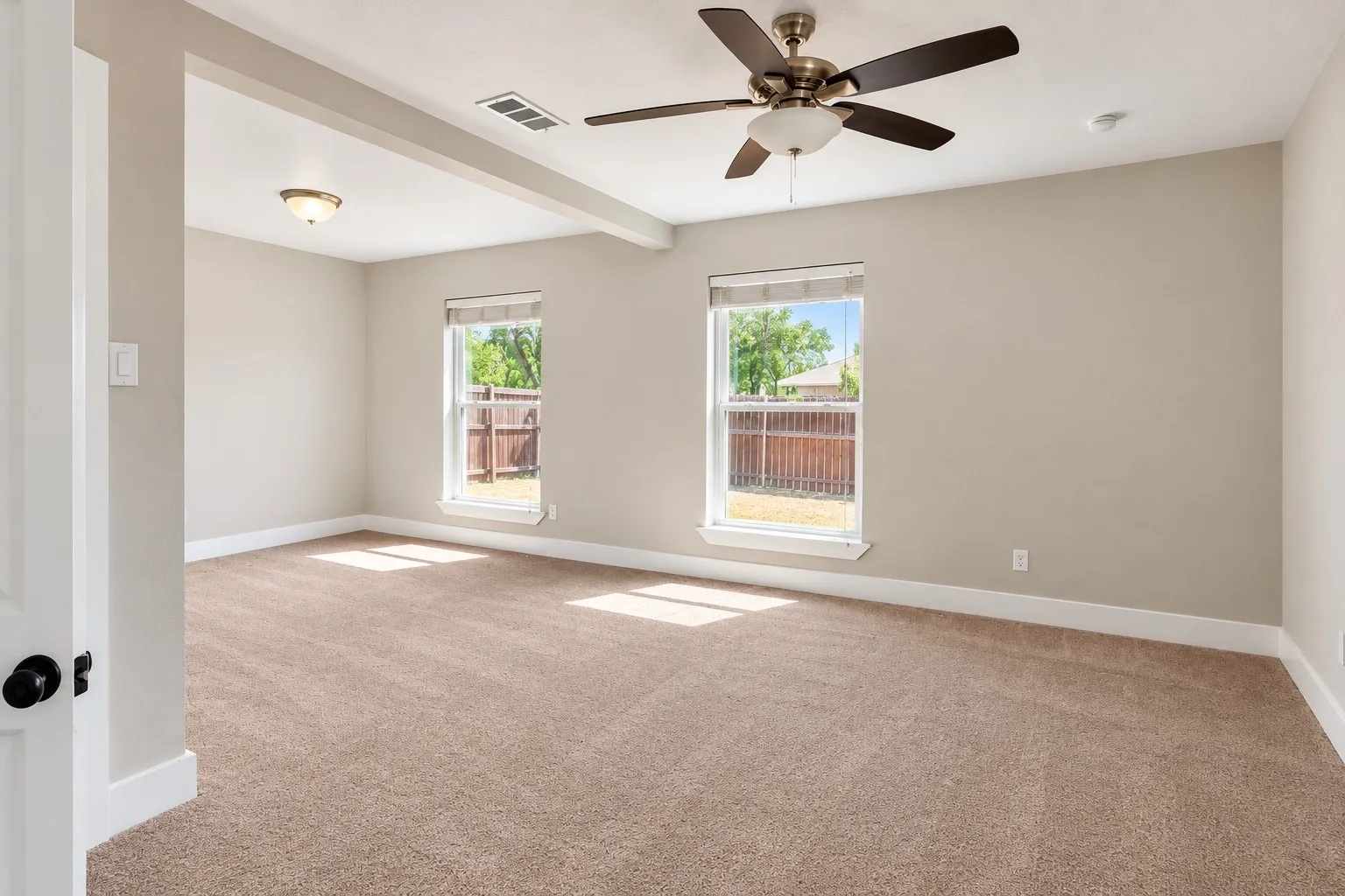 Carpeted flooring, neutral wall tones, two windows with white trim, and a ceiling fan with integrated lighting