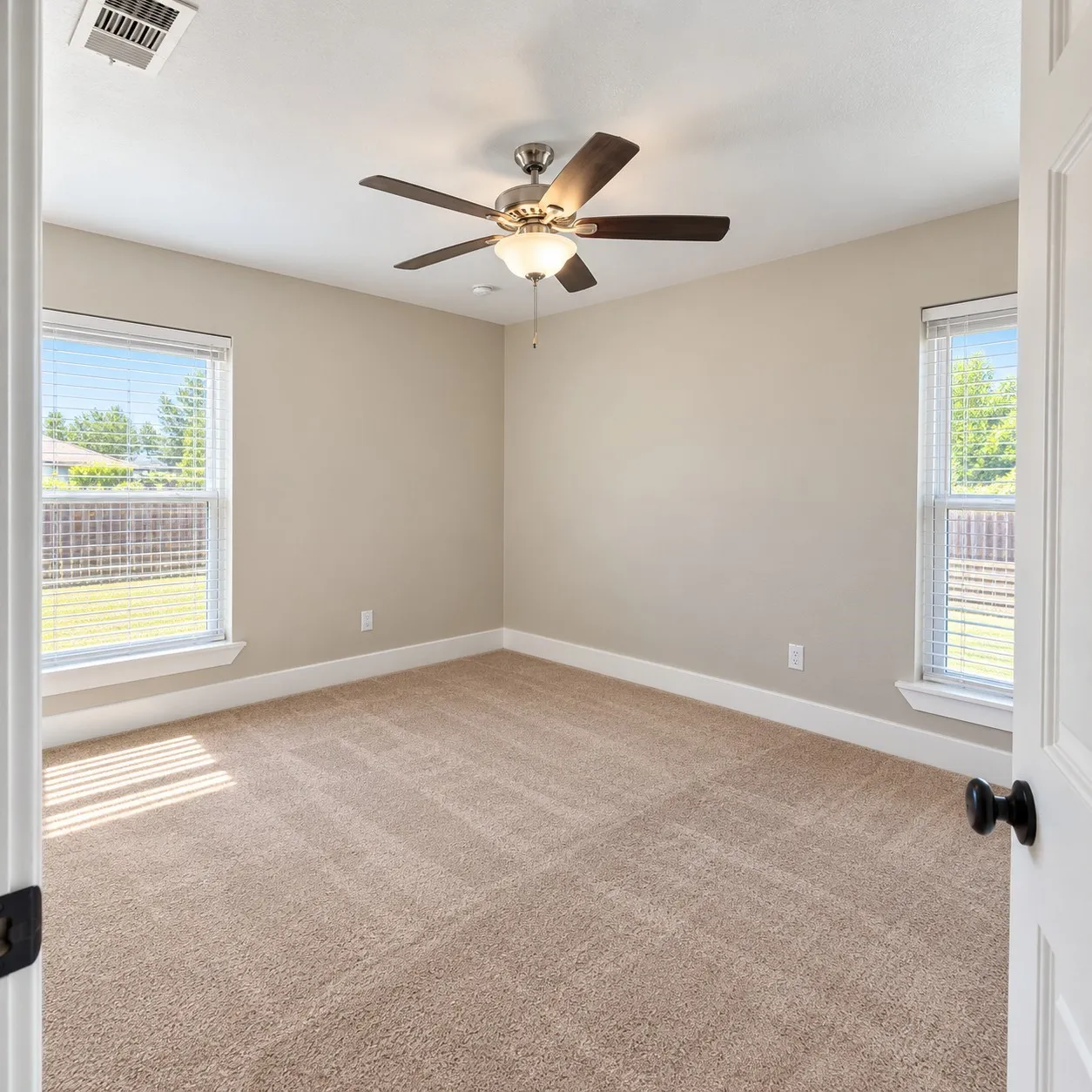 Neutral wall finishes, plush carpeting, two windows with blinds, and a ceiling fan with integrated lighting