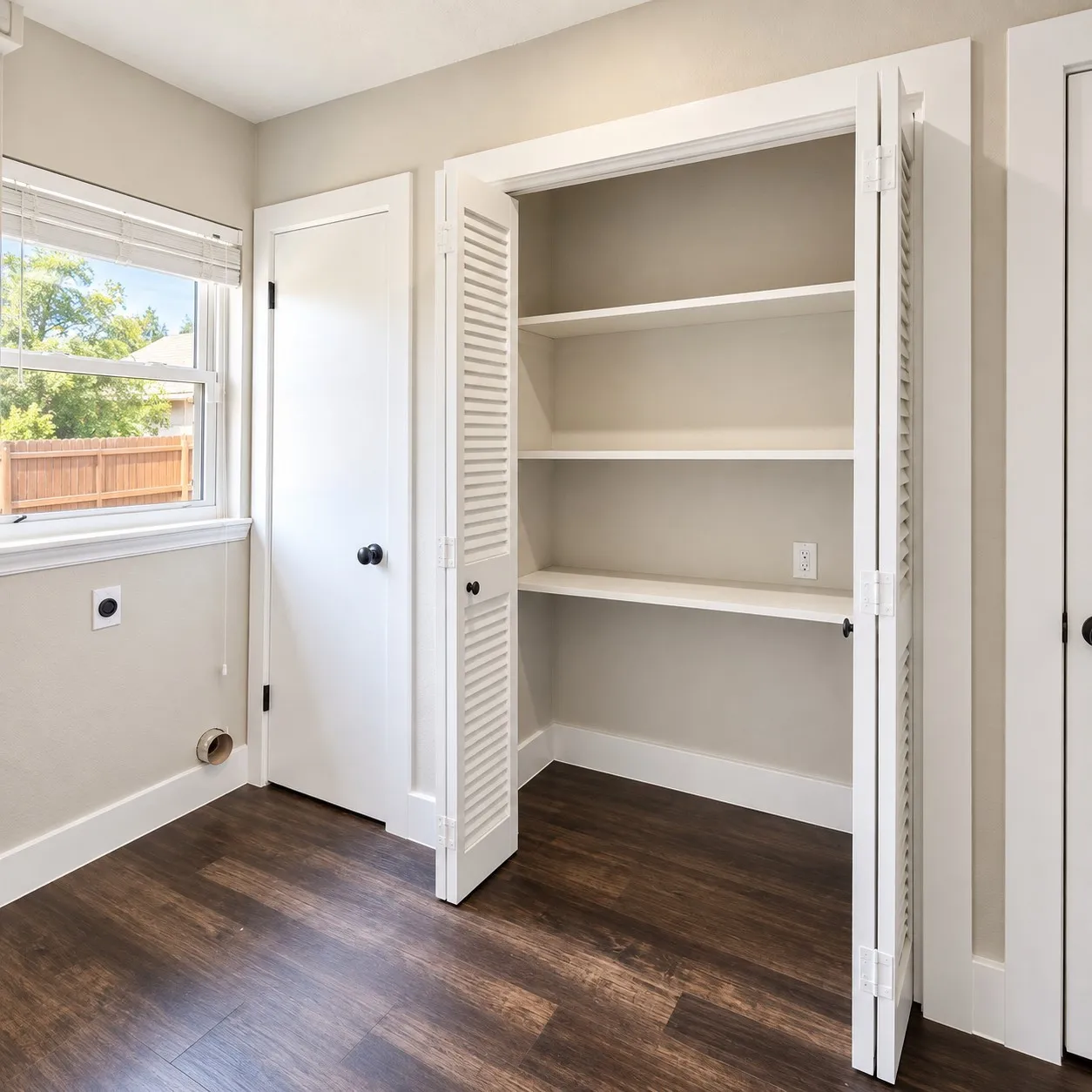 Wood-finish flooring, built-in shelving, louvered closet doors, and a window with blinds
