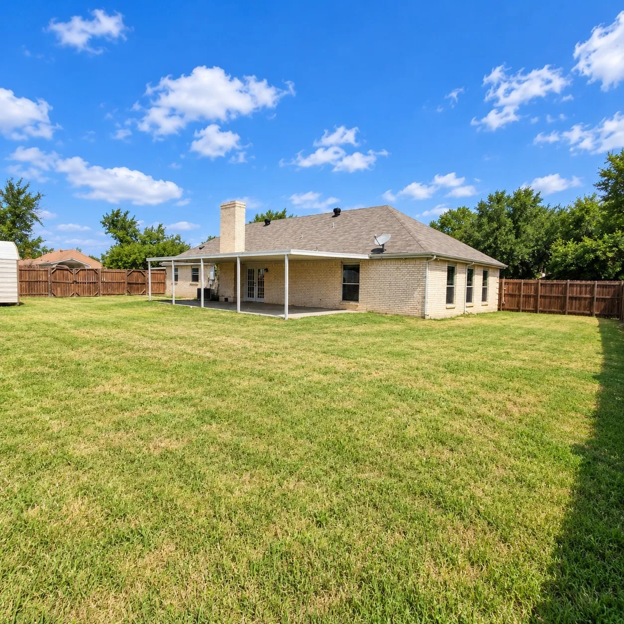 Expansive backyard with a manicured lawn, full privacy fencing, and a covered patio area
