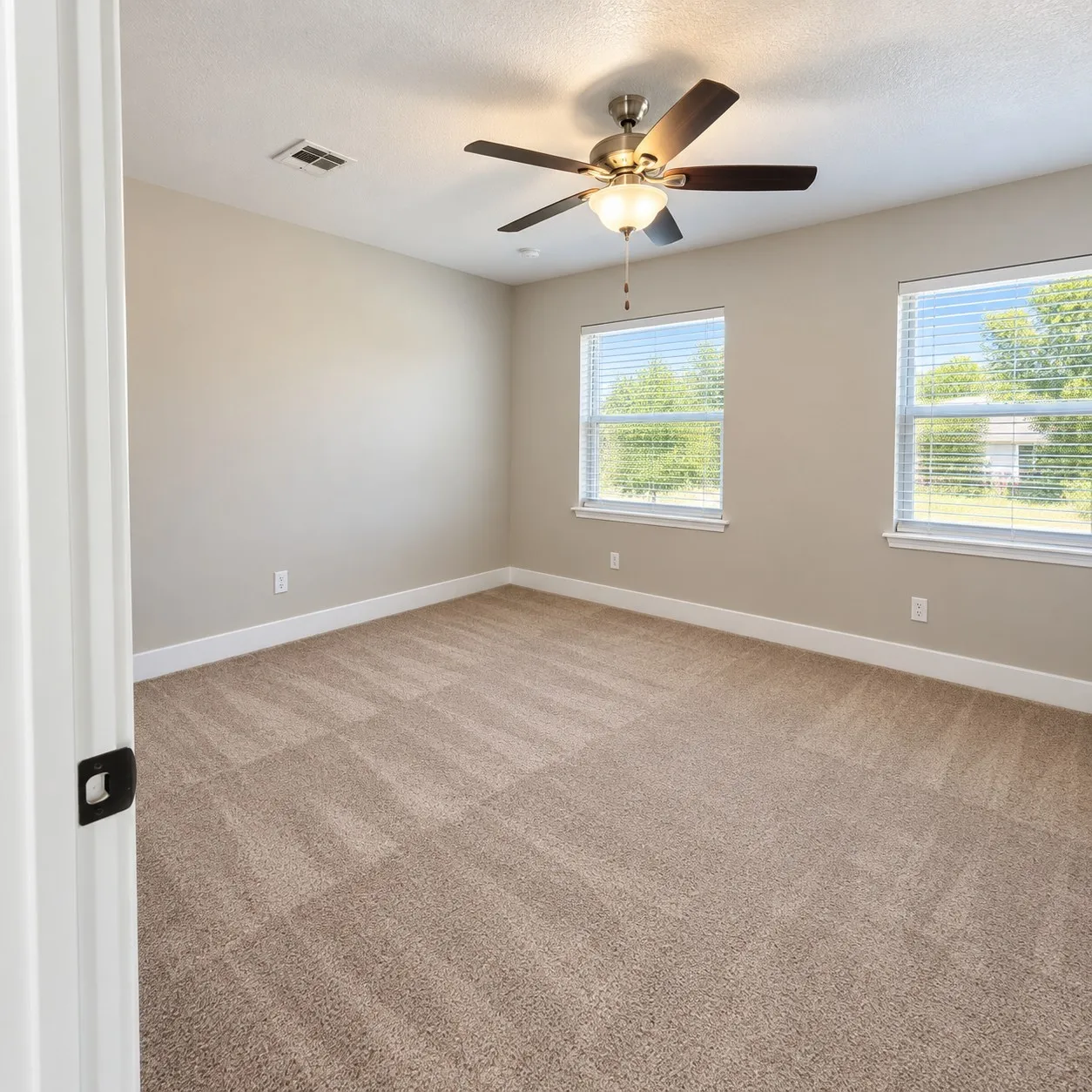 Neutral-toned carpeting, two large windows with blinds, a ceiling fan with integrated lighting, and light-colored walls