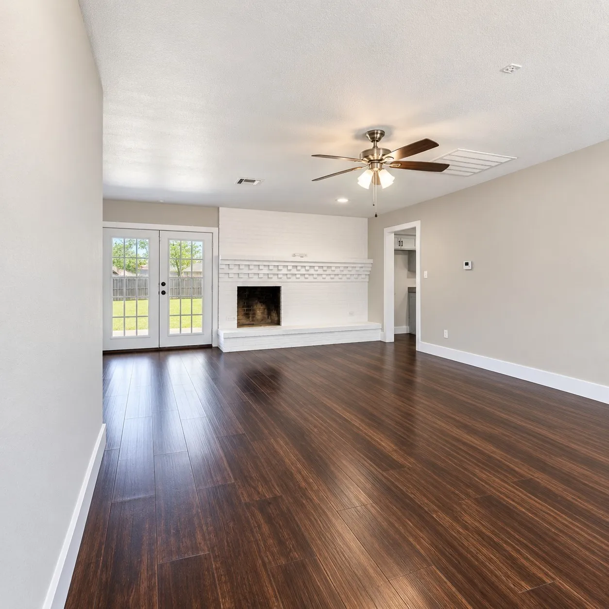 Wood-laminate flooring featuring a white brick fireplace, white trim, and a ceiling fan
