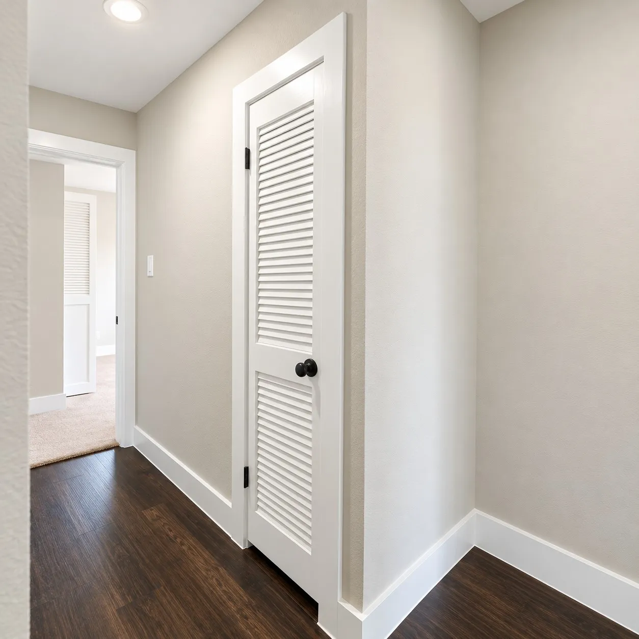 Recessed ceiling lighting, wood-finish flooring, white louvered door, black hardware, white trim