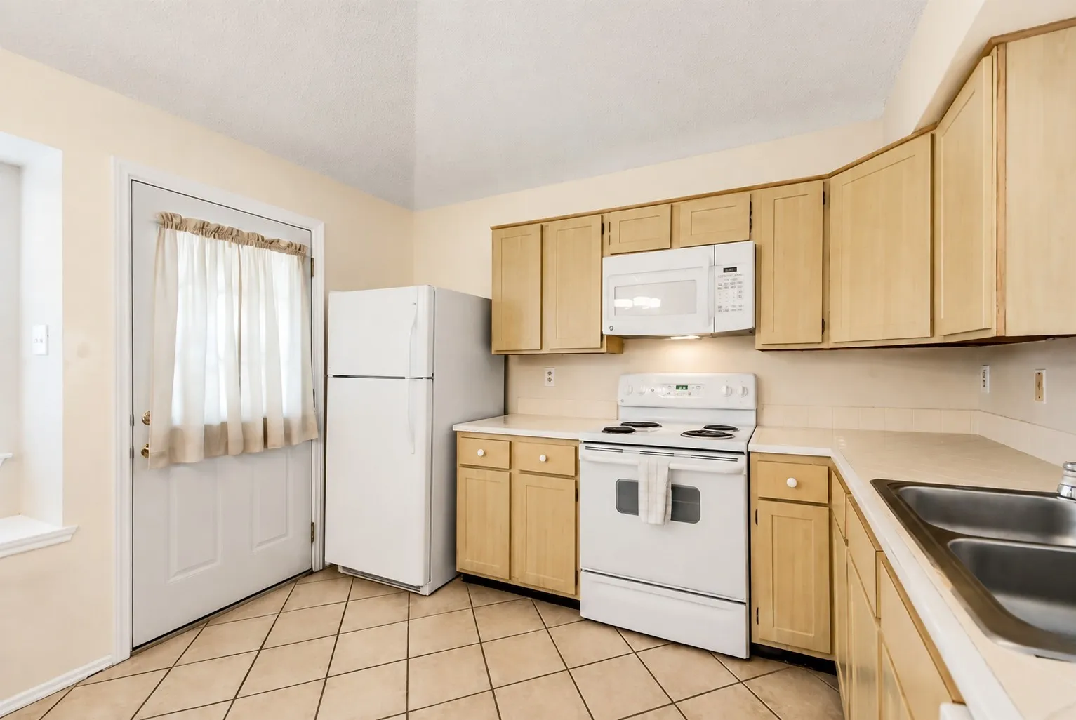 Kitchen featuring tile flooring, wood-finish cabinetry, white appliances, and a double basin sink