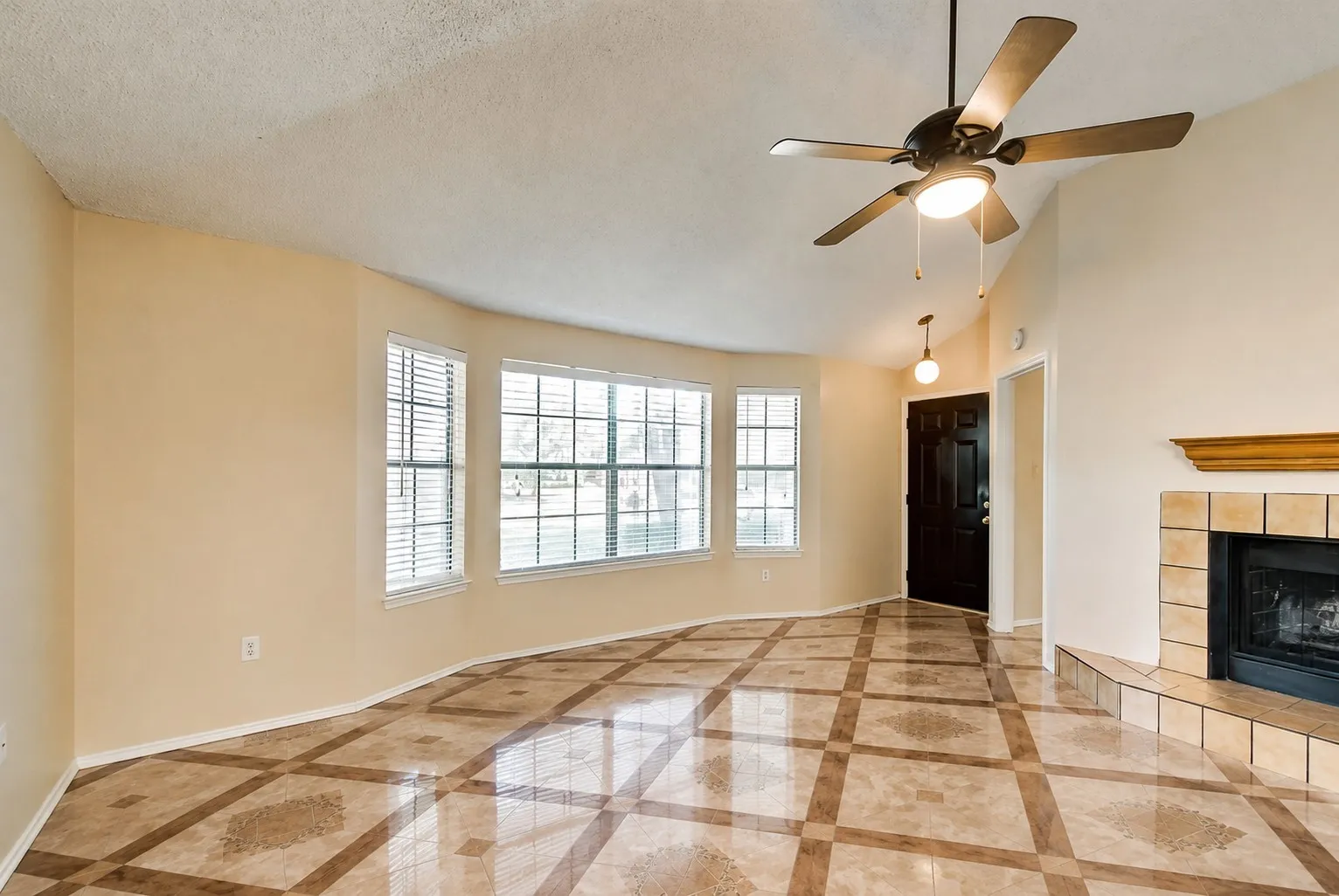 Living area with patterned tile flooring, a bay window with blinds, a ceiling fan with integrated lighting, and a fireplace with a tile surround and mantel