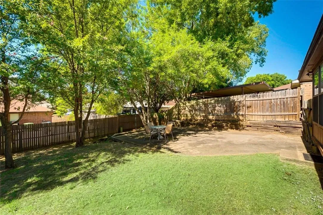 Expansive yard featuring a concrete patio, grassy area, mature trees, and wood fencing