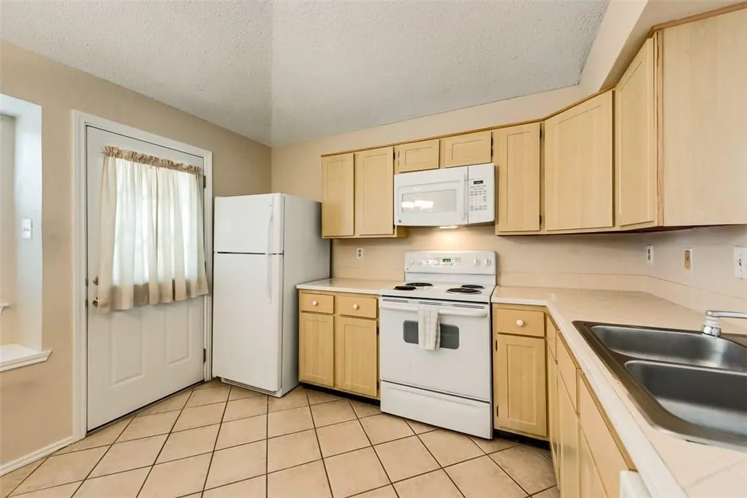 Kitchen featuring neutral-toned cabinetry, tile flooring, white appliances, and a double basin sink