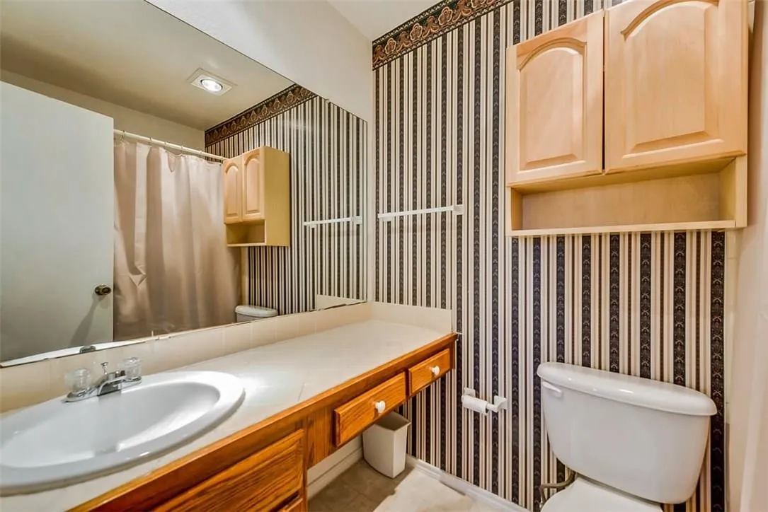 Vanity with integrated sink, wood-finish cabinetry, full-width mirror, and overhead lighting