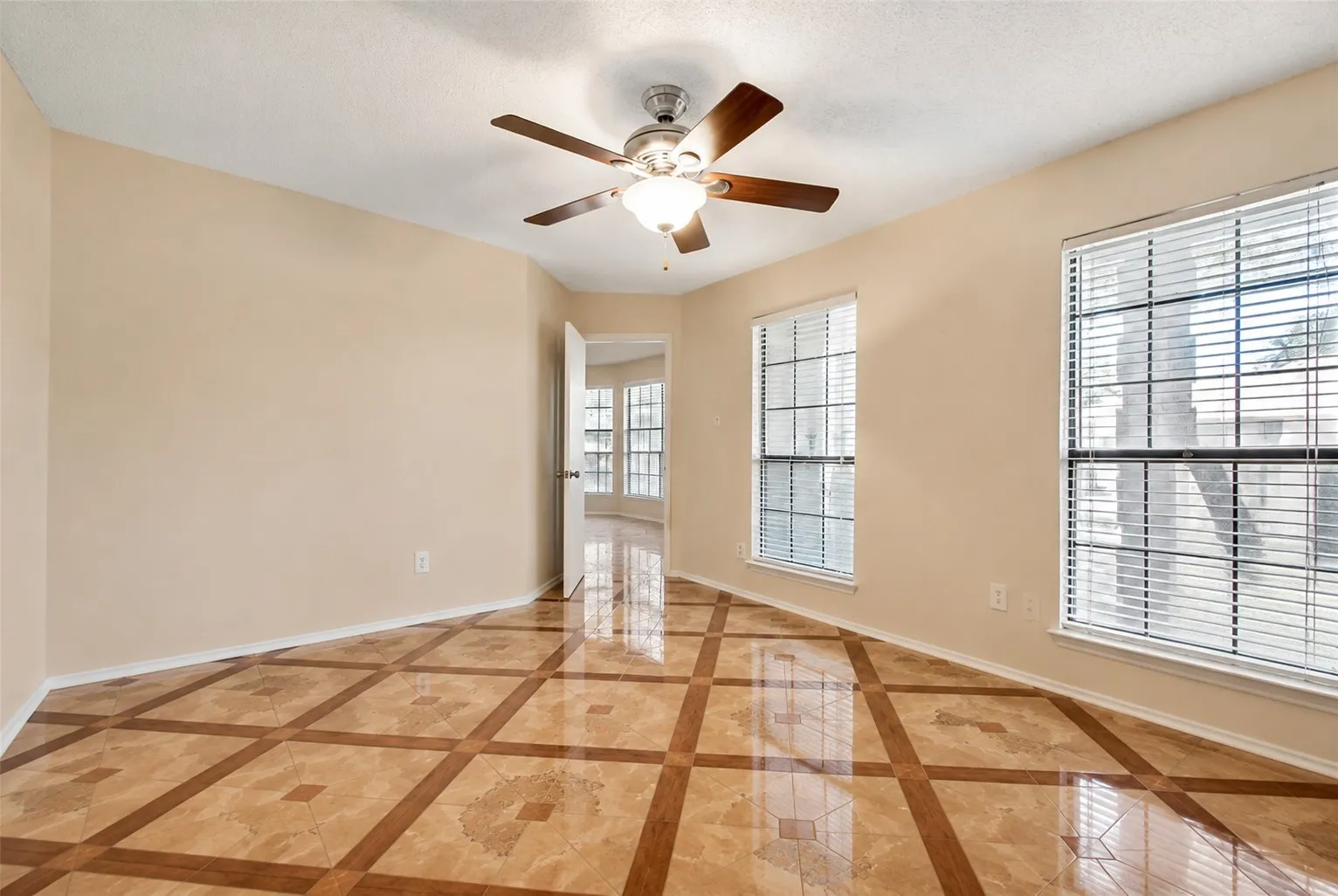 Patterned tile flooring, ceiling fan with integrated lighting, two windows with blinds, and neutral wall tones