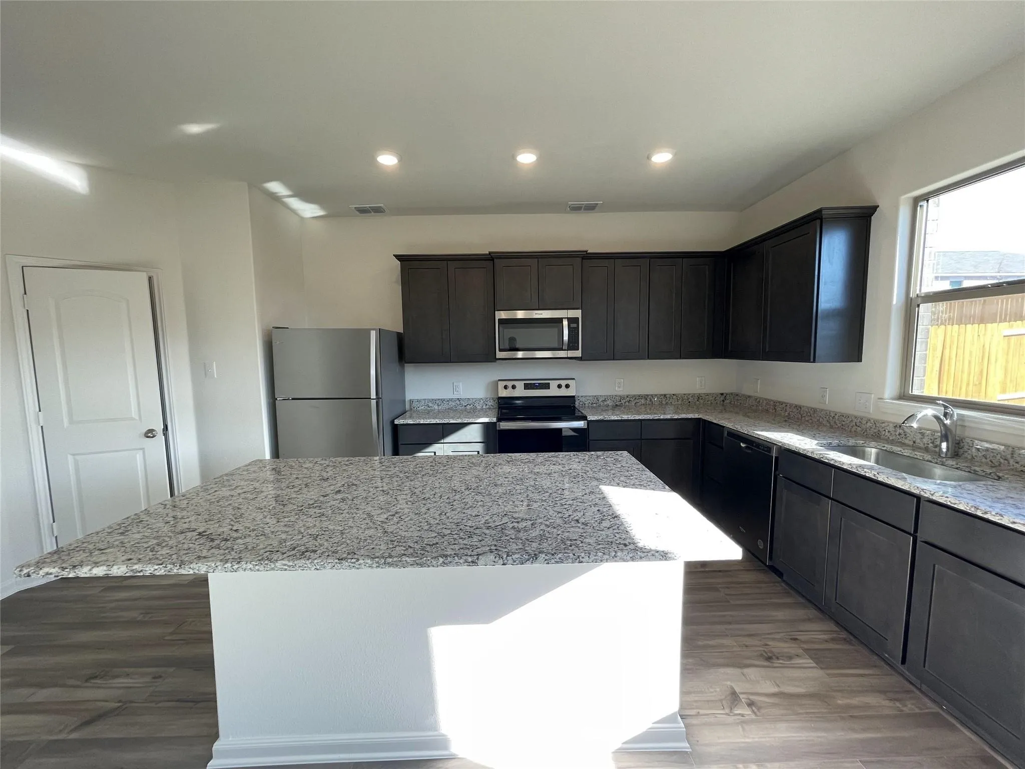 Kitchen featuring an island with stone countertops, dark wood-finish cabinetry, stainless steel appliances, and wood-finish flooring