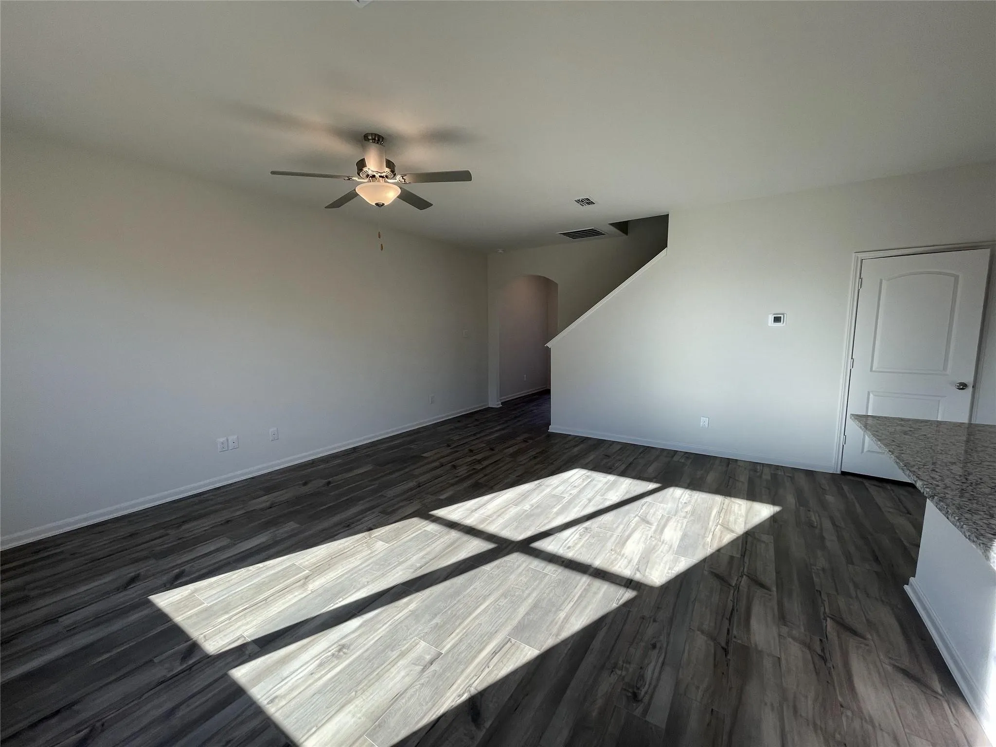 Spacious open-concept room featuring wood-finish flooring, a ceiling fan with integrated lighting, and a white paneled door