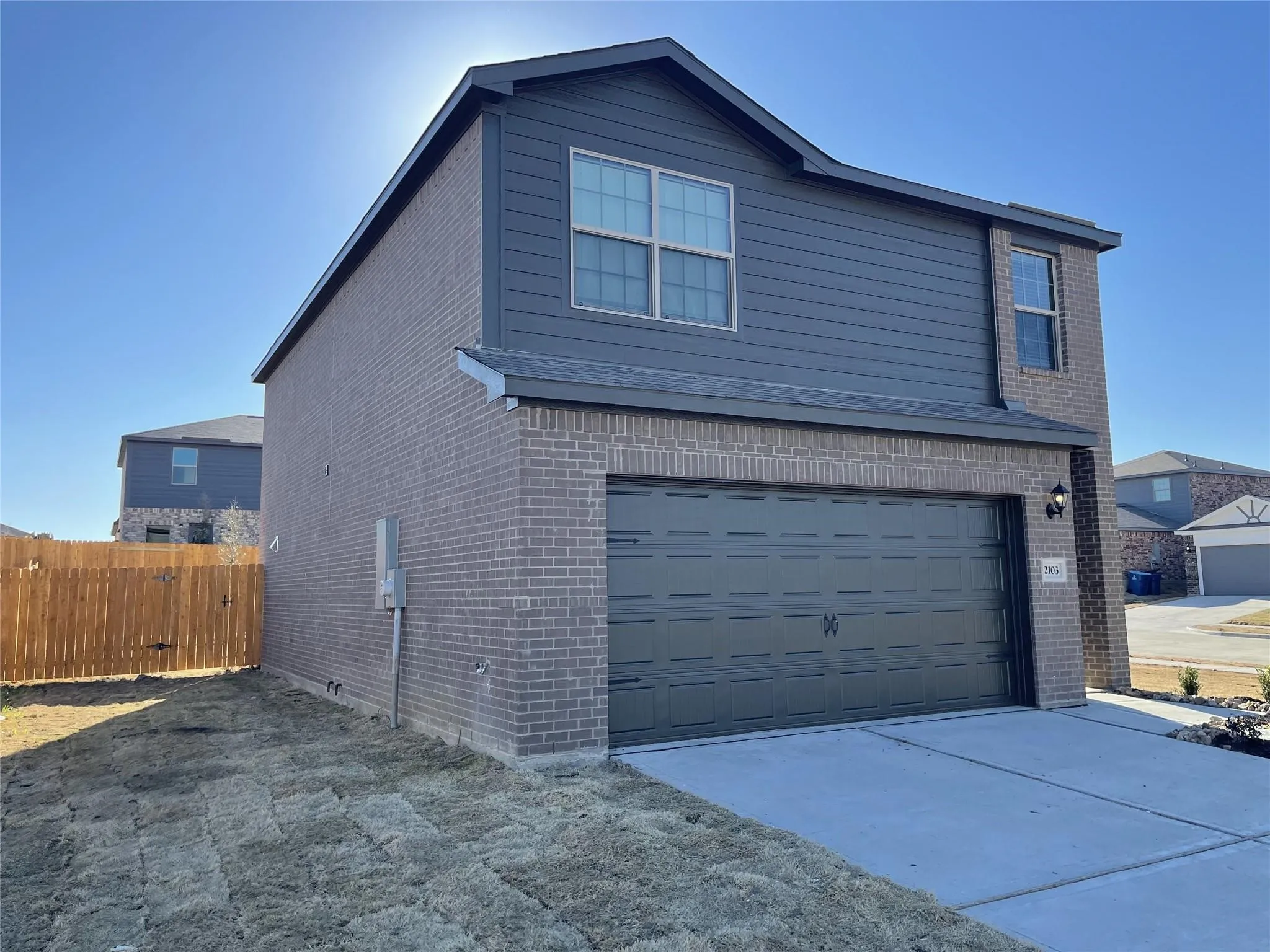 Two-story residence featuring a brick and horizontal siding exterior, attached two-car garage, concrete driveway, and a wood privacy fence