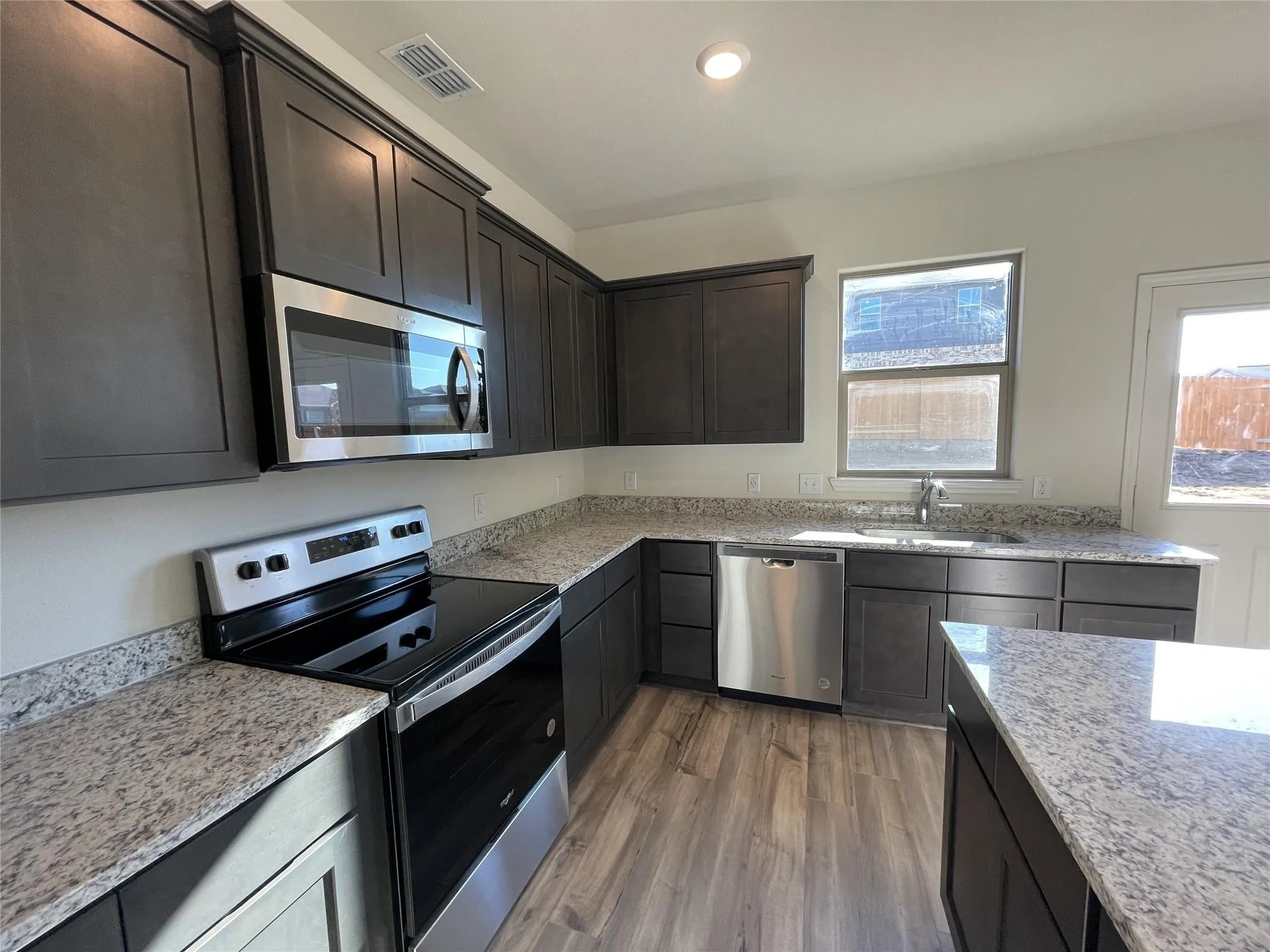 Kitchen featuring dark wood-finish cabinetry, light-toned countertops, stainless steel appliances, and wood-look flooring