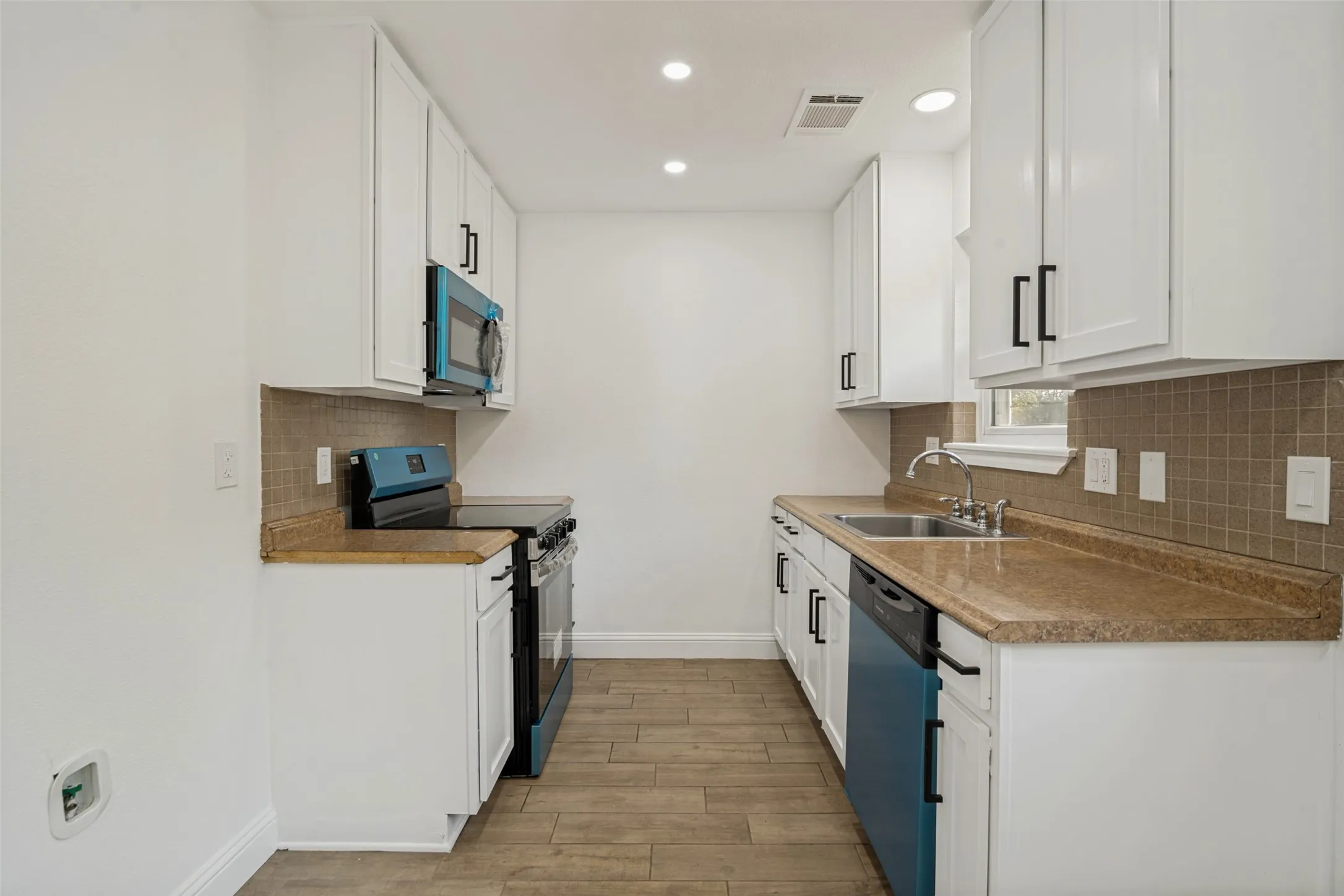 White cabinetry with matte black hardware, light brown countertops, and a tiled backsplash