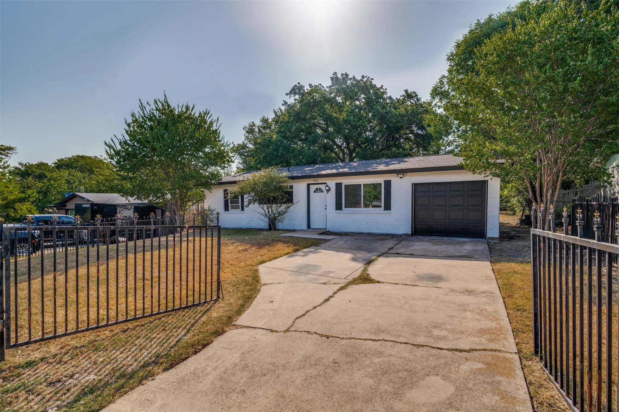 White brick exterior with dark shutters, attached single-car garage, and a black wrought iron fence