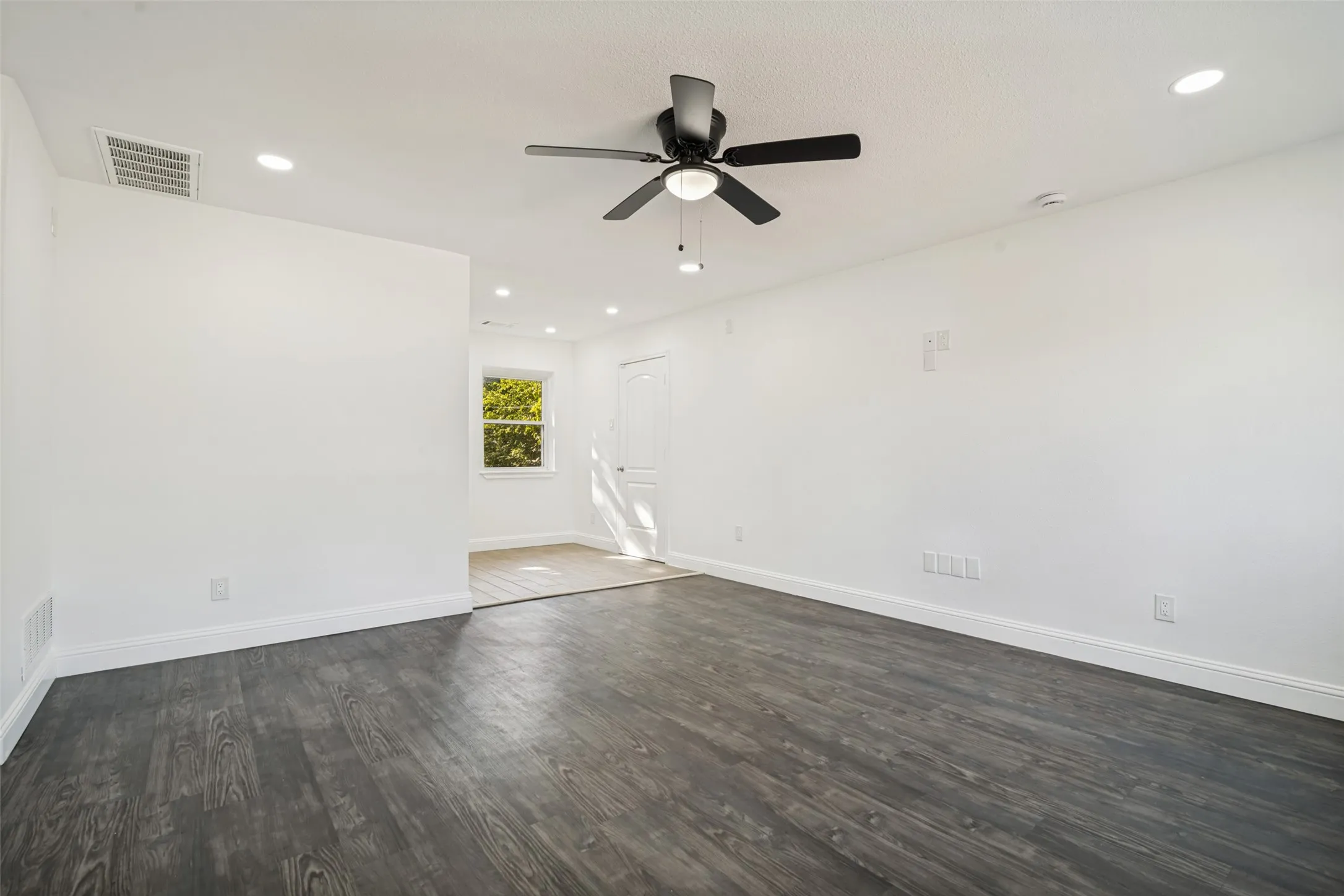 Recessed lighting, dark wood-finish flooring, white painted walls, a window, and a ceiling fan with integrated lighting