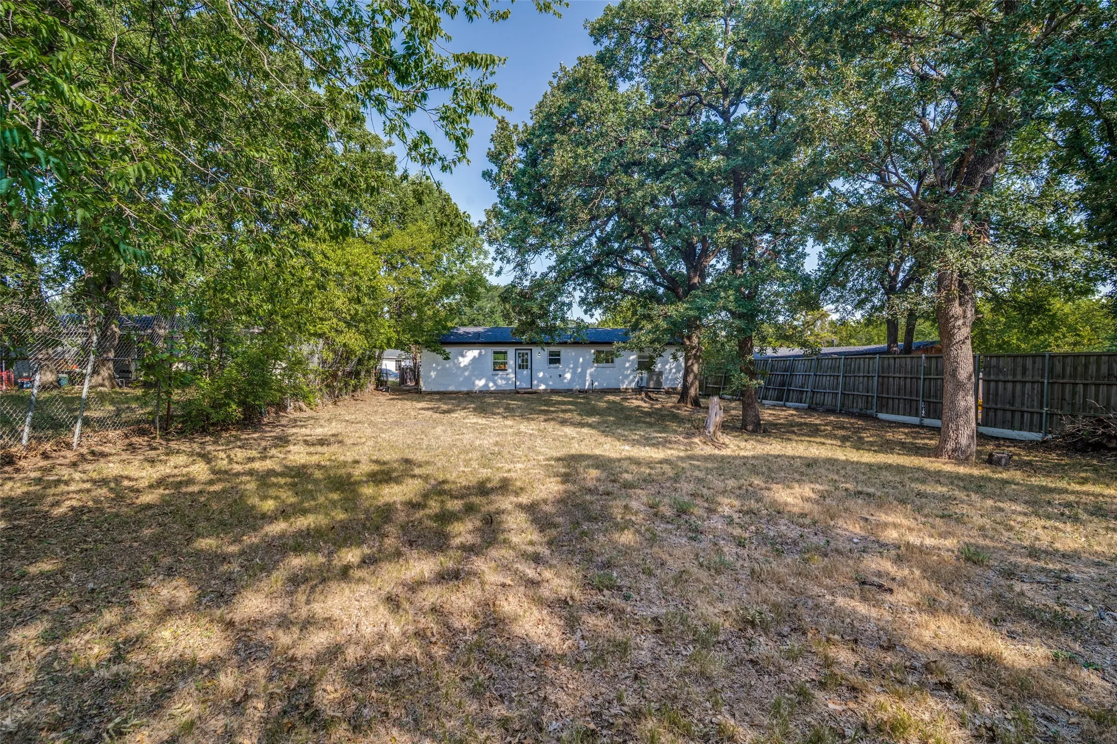 Expansive rear yard featuring mature trees, a wood privacy fence, and a chain-link fence