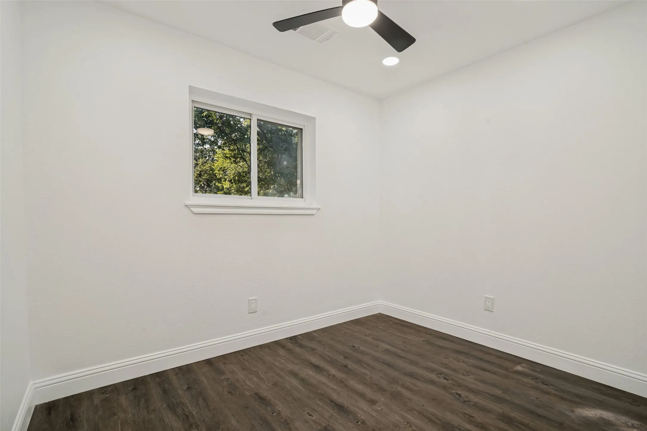 Contemporary ceiling fan, recessed lighting, wood-finish flooring, white trim, and a window with a green exterior