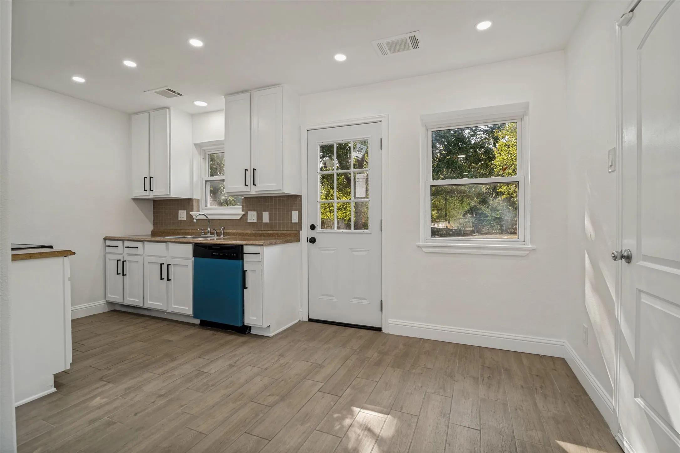 Kitchen featuring white cabinetry, light-toned wood-finish flooring, recessed lighting, a tile backsplash, and a glass-paneled exterior door