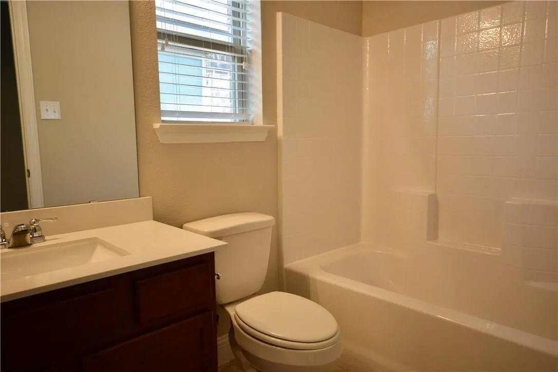 White bathtub and shower combination with integrated shelving, dark wood-finish vanity with a single basin sink, and a mirrored wall