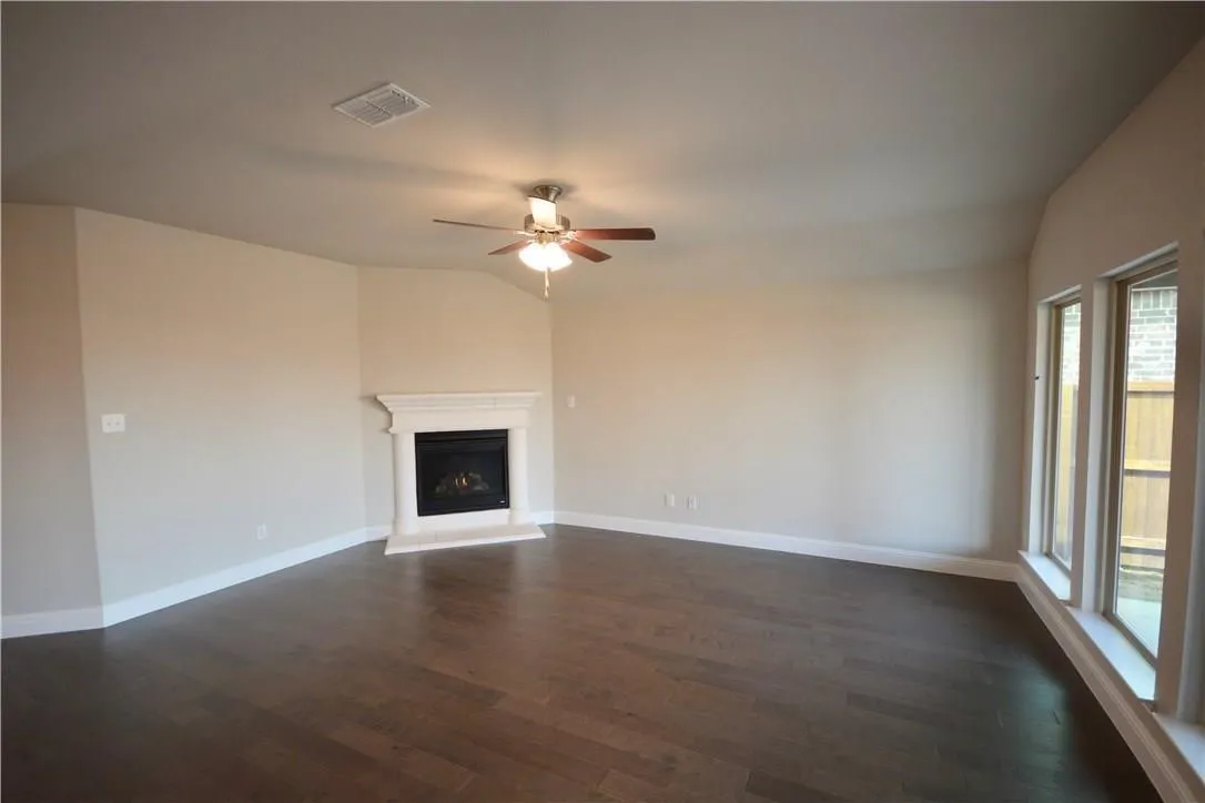Vaulted ceiling with a ceiling fan, fireplace with a white mantel, three large windows, and wood-finish flooring