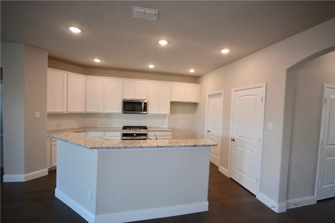 Kitchen featuring white cabinetry, granite countertops, stainless steel microwave, and recessed lighting