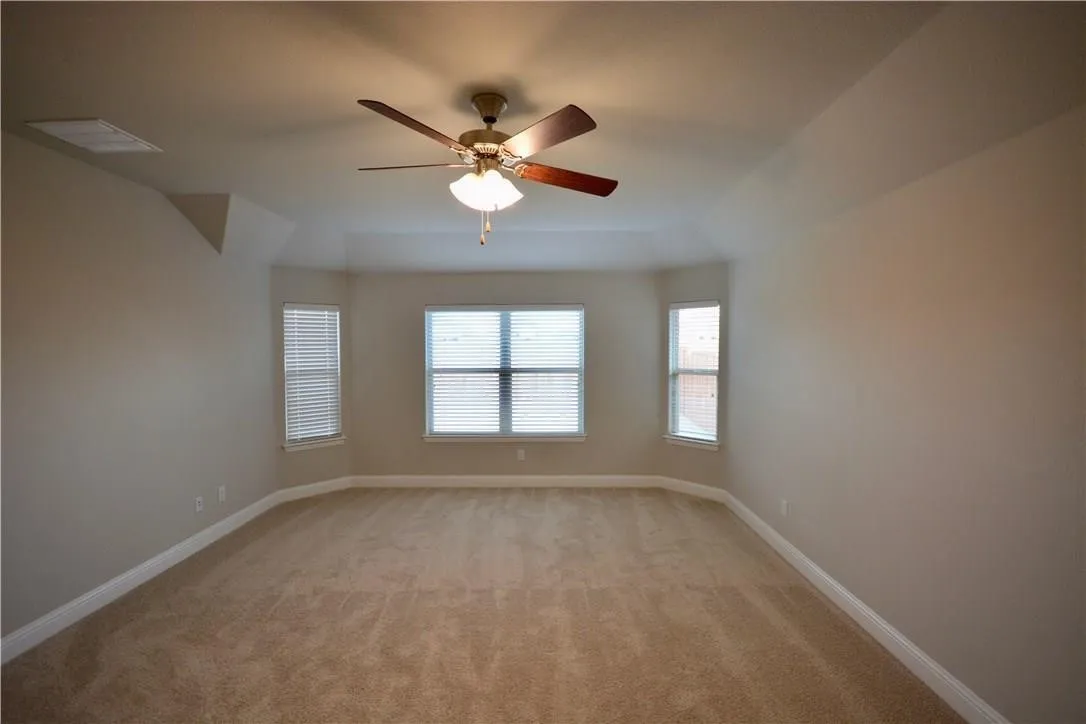 Tray ceiling with a ceiling fan, bay window with blinds, and neutral carpeting