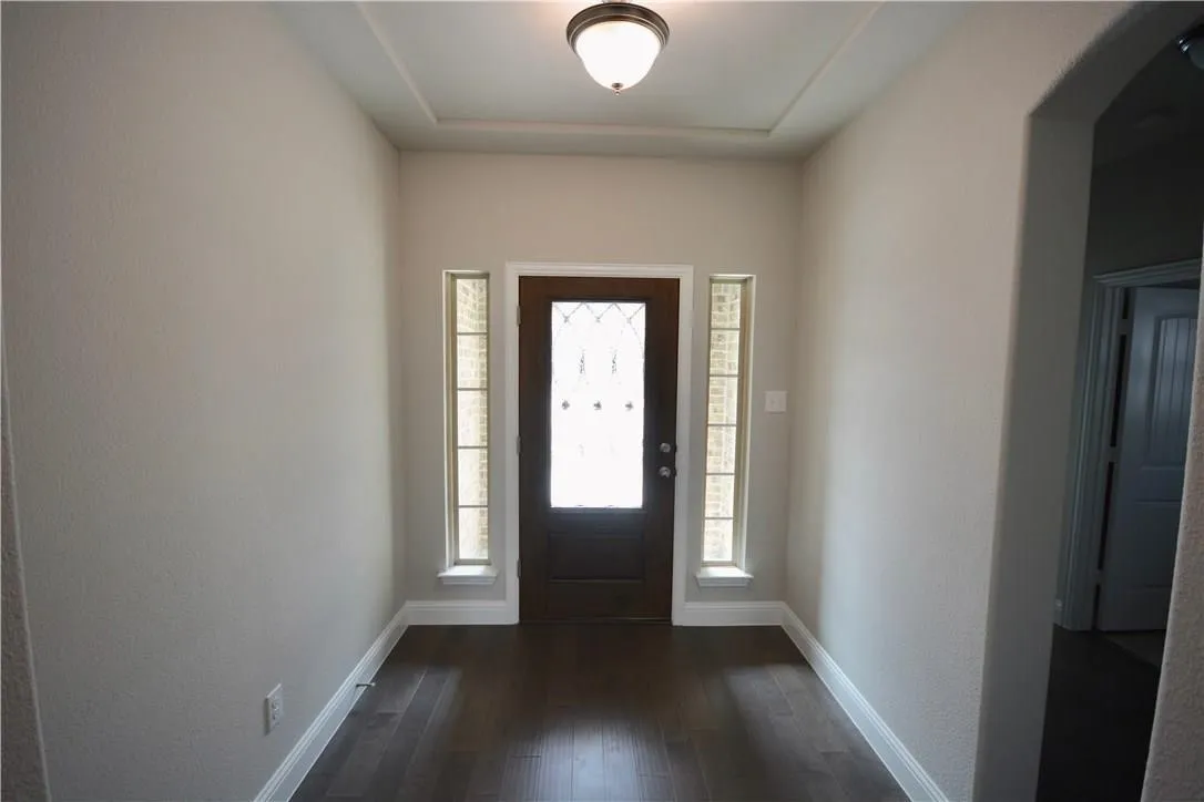 Rich wood-finish flooring with a decorative entry door featuring leaded glass, framed by two sidelight​​‌​​​​‌​​‌‌​‌‌​​​‌‌​‌​‌​‌​​​‌​​ windows