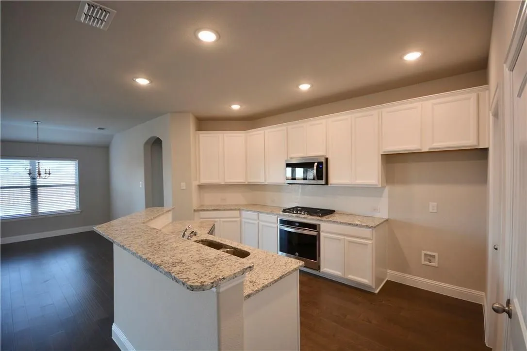 Kitchen featuring white cabinetry, granite countertops, stainless steel appliances, and wood-finish flooring