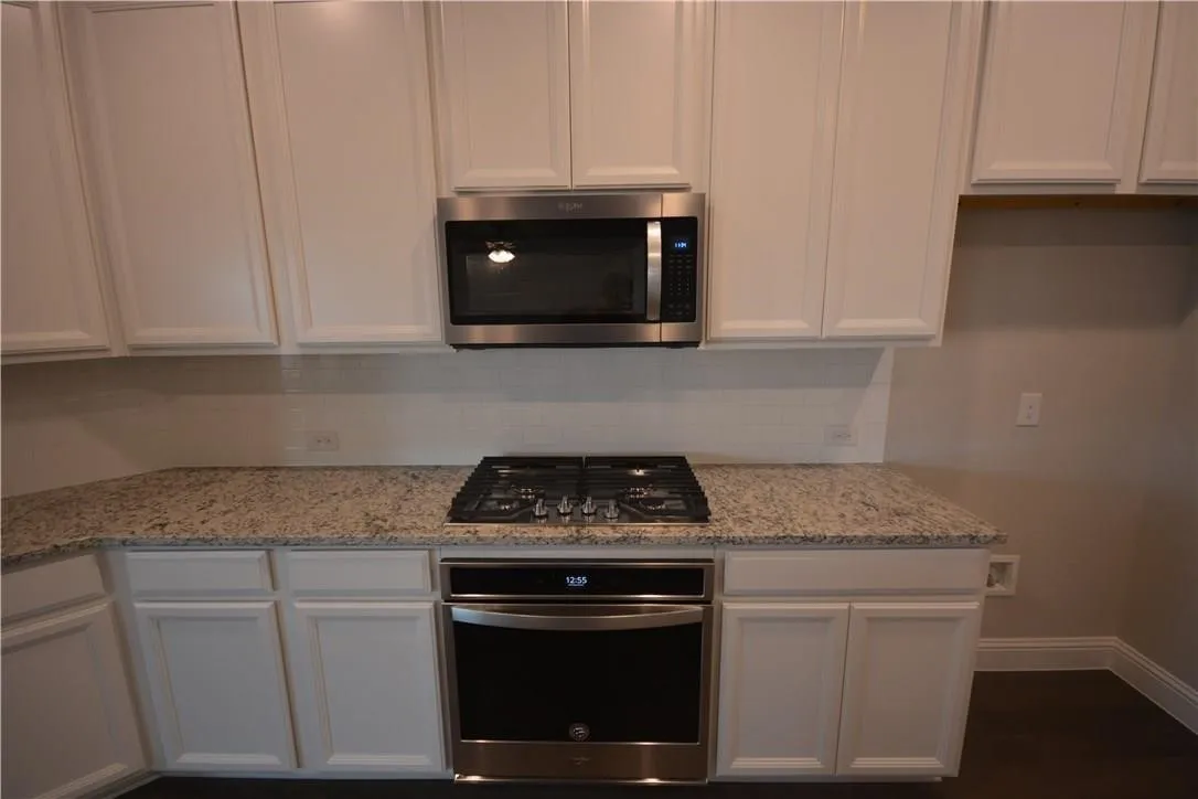 Modern kitchen featuring white shaker-style cabinetry, granite countertops, stainless steel gas cooktop, matching stainless steel microwave and wall oven, and neutral tile backsplash