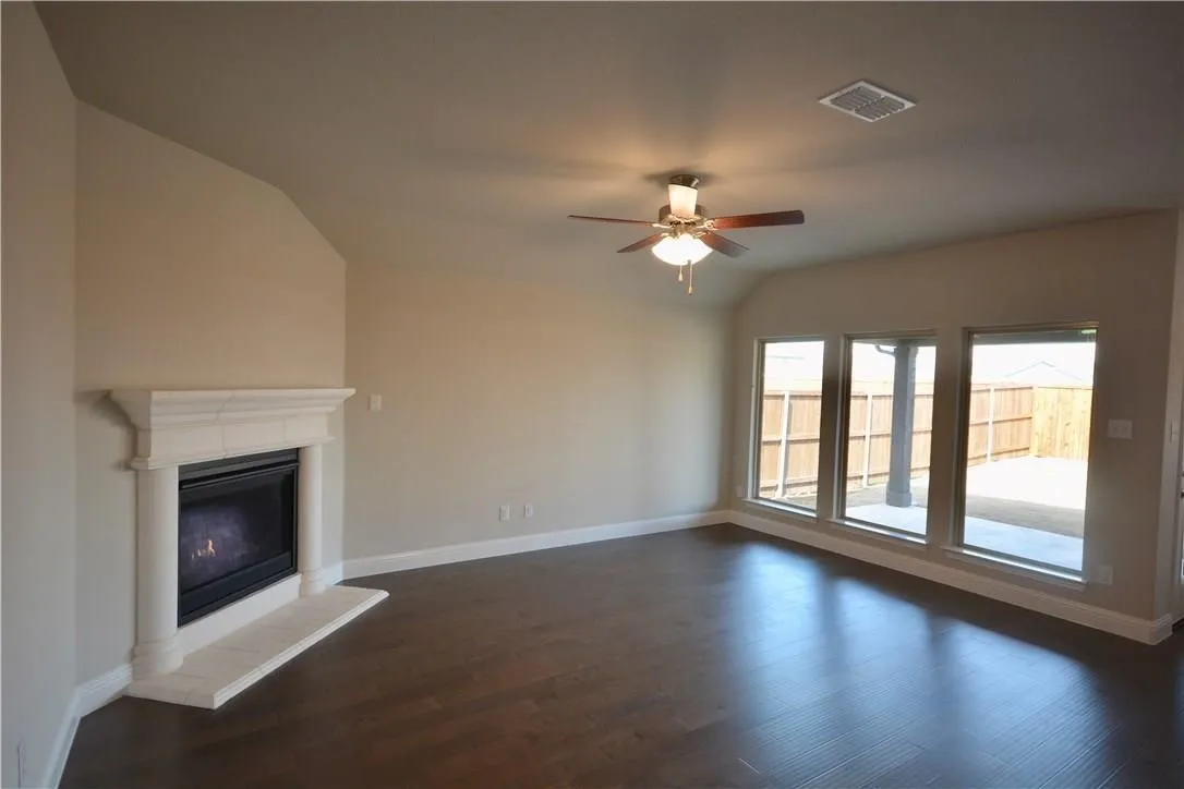 Wood-finish flooring, white mantel fireplace, three large windows, recessed lighting, and a ceiling fan with integrated lighting