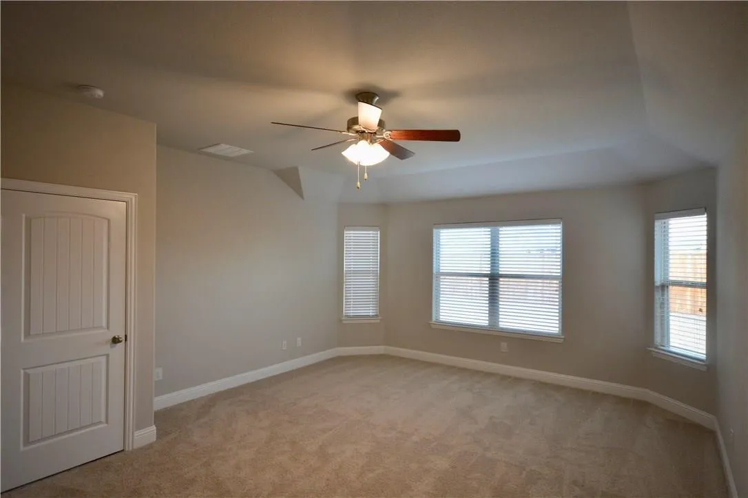 Spacious carpeted room with a ceiling fan, multiple windows, and a paneled door
