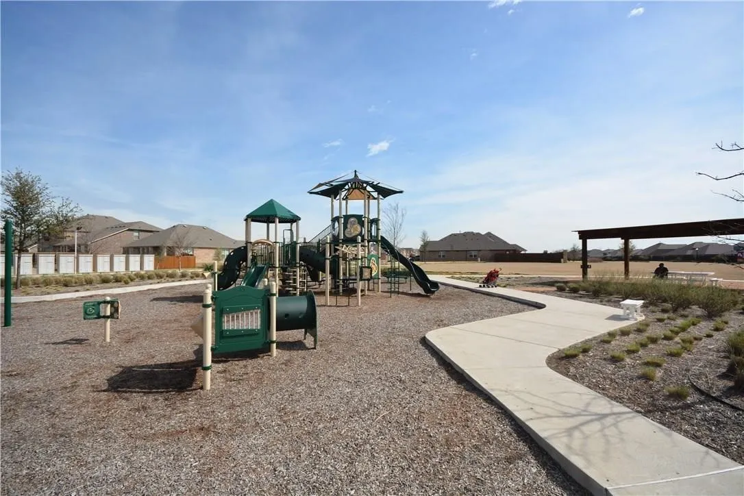 Community playground with multiple play structures, a winding concrete pathway, and an open-air pergola