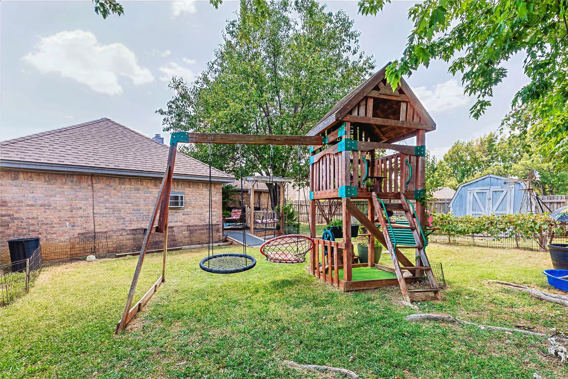 Expansive backyard featuring a manicured lawn, mature trees, and a wooden play structure