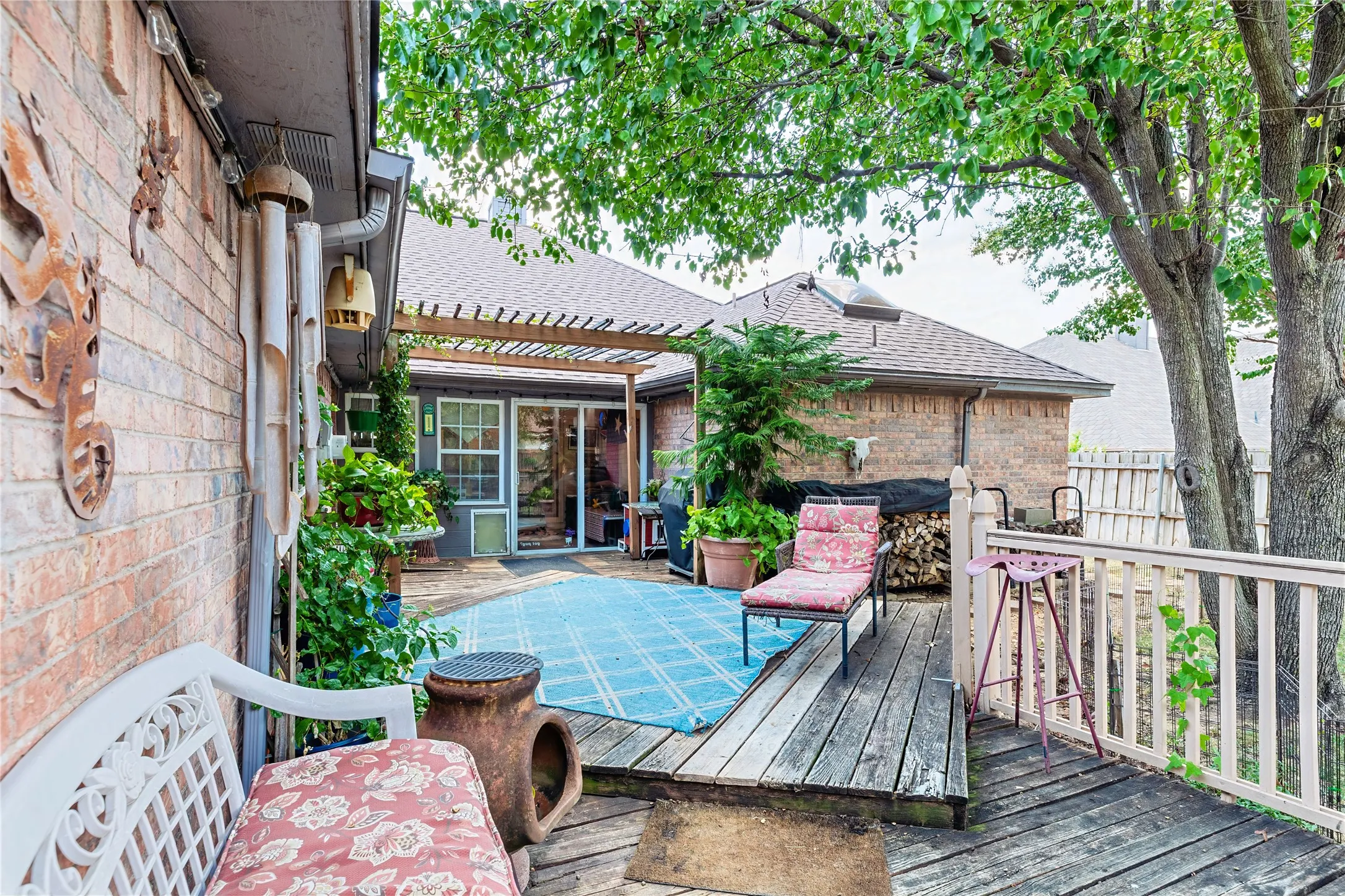 Brick exterior with a wood deck, pergola, privacy fence, and mature trees