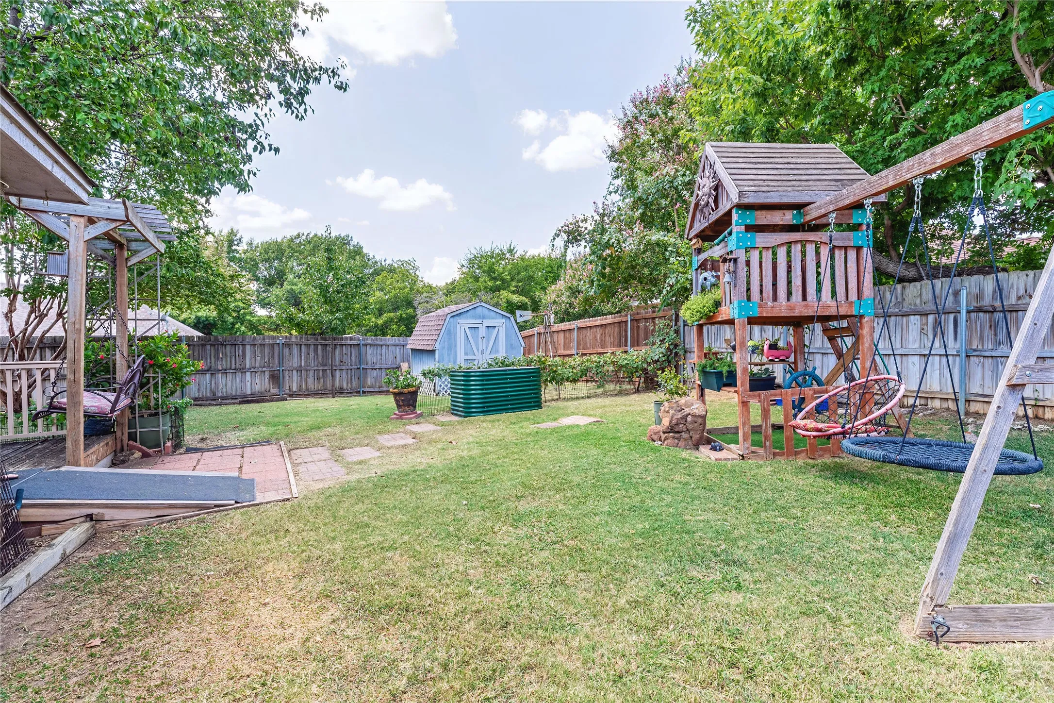 Expansive backyard featuring a manicured lawn, a wooden privacy fence, a detached storage shed, and a raised pergola structure