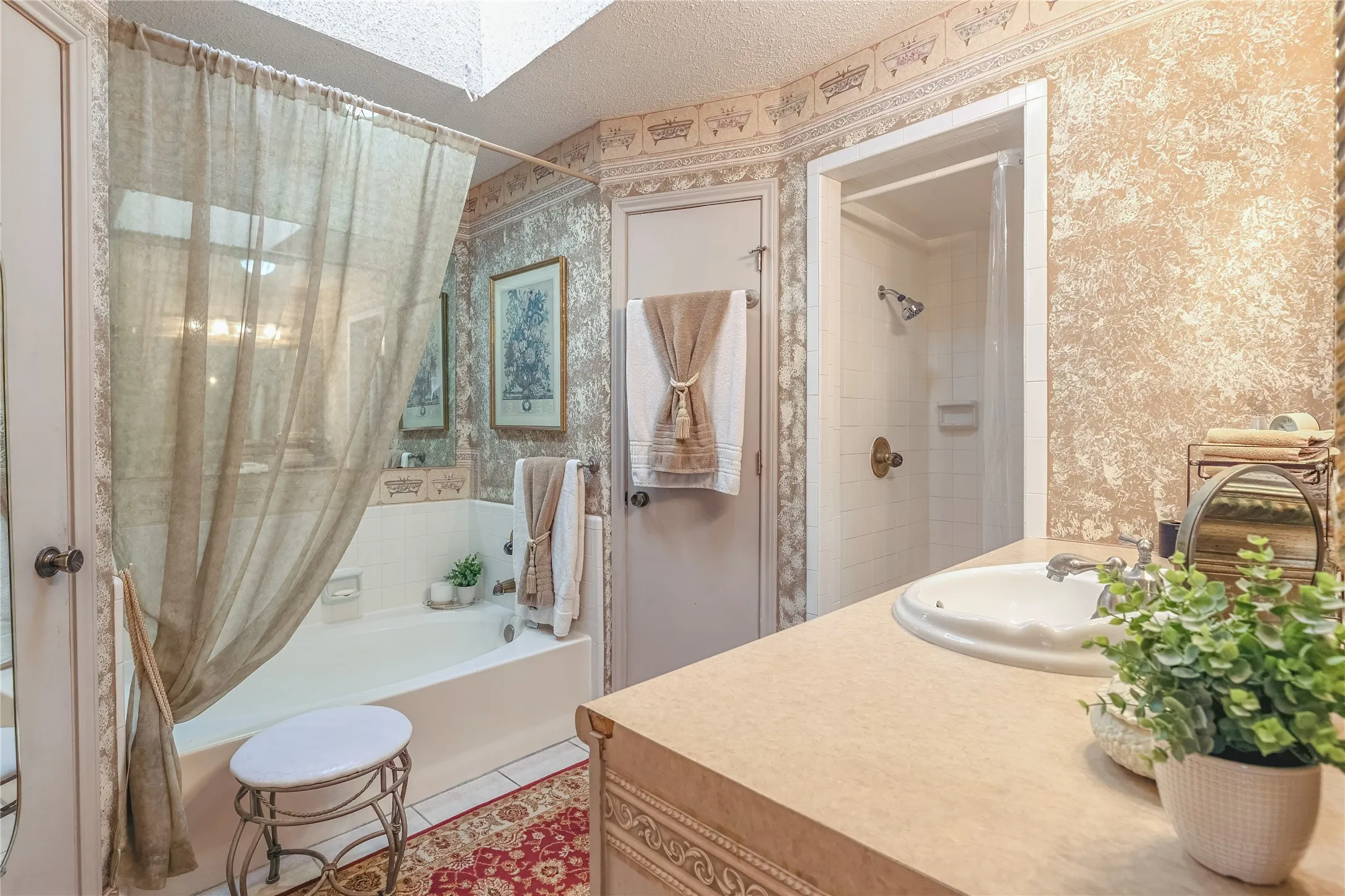 White soaking tub with skylight, single vanity with integrated sink, and enclosed shower