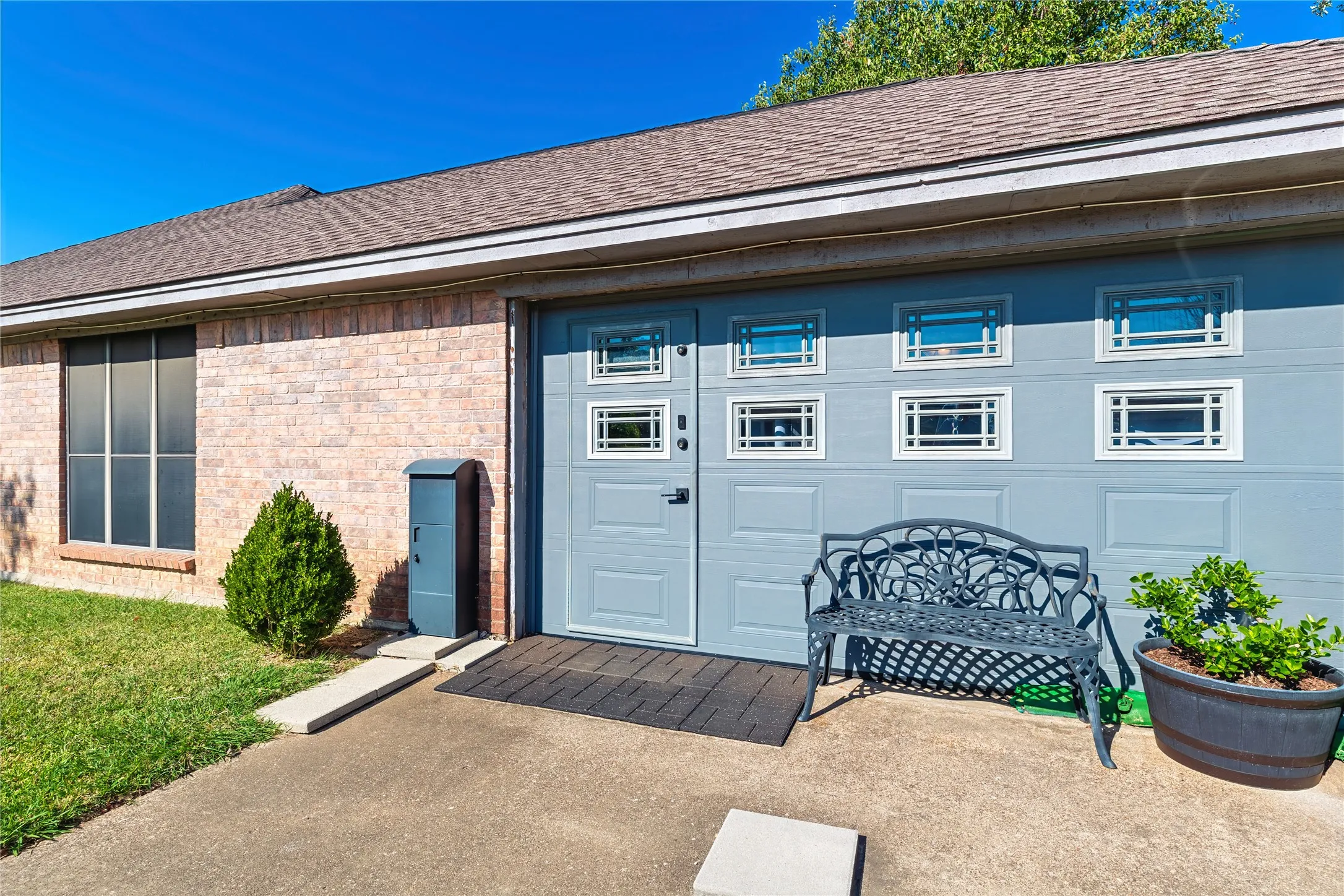 Brick exterior with a shingled roof, featuring a garage door with window inserts, and a large front window