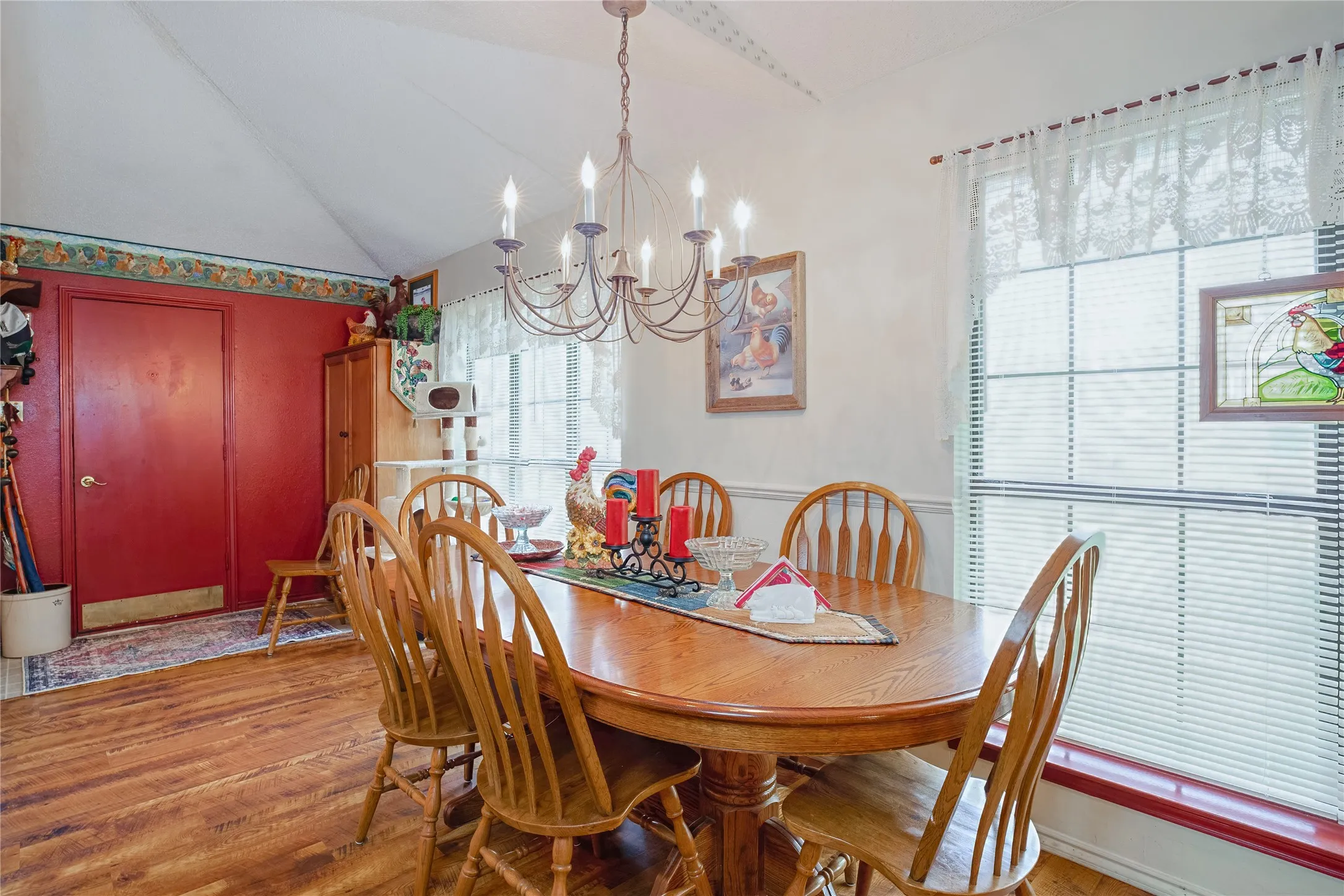 Vaulted ceiling with an ornate chandelier, wood-finish flooring, and a large window with horizontal blinds
