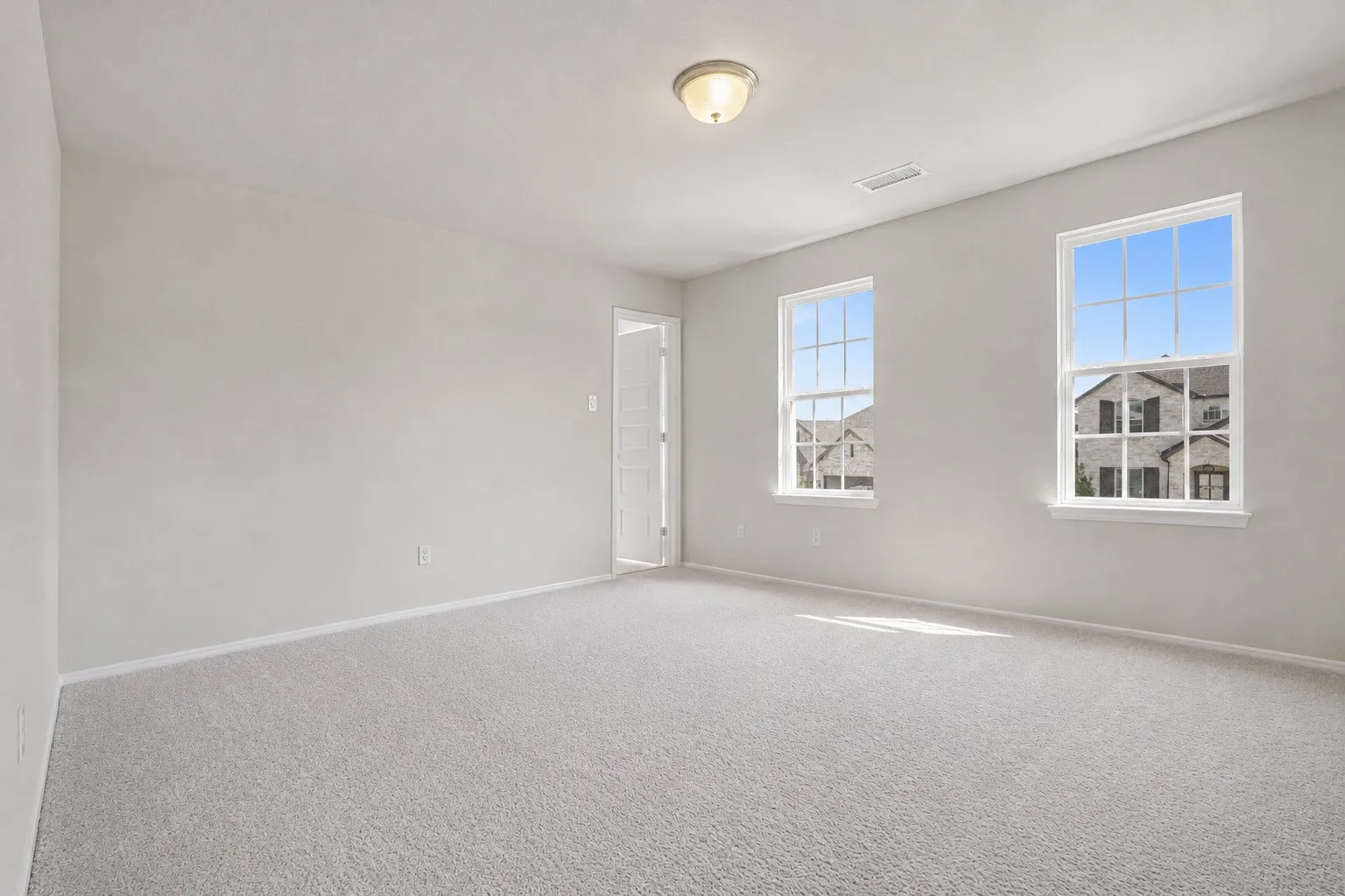 Neutral wall finish, light-colored carpeting, two double-hung windows, and a flush mount ceiling light fixture