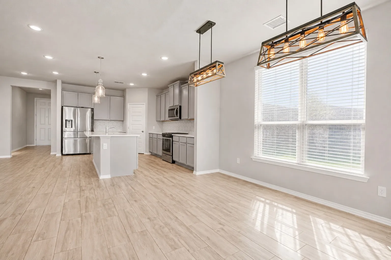 Wood-finish flooring throughout, kitchen island with built-in sink, stainless steel appliances, recessed lighting, and industrial-style pendant lighting fixtures