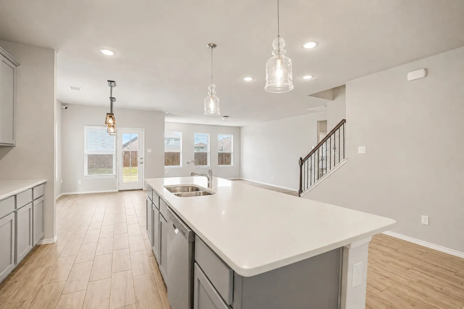 Open-concept kitchen with a large island, white countertops, gray cabinetry, and wood-finish flooring
